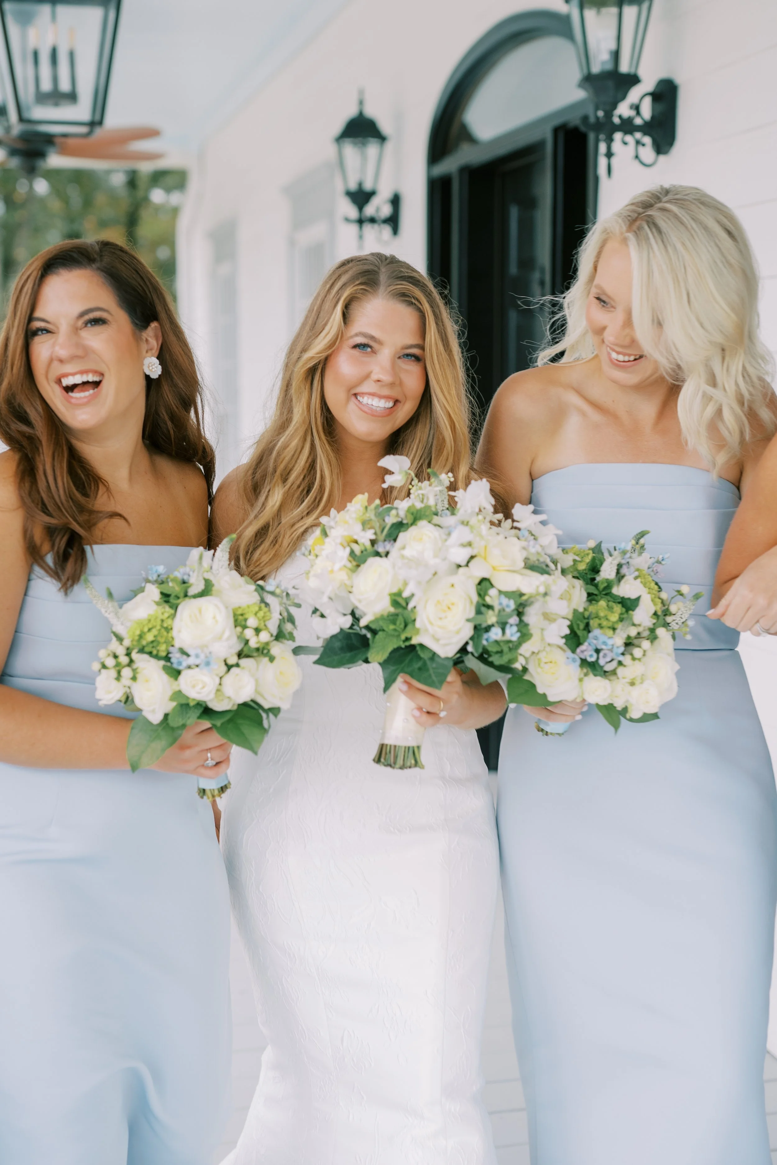 Bridesmaids in light blue dresses smiling with their bouquets
