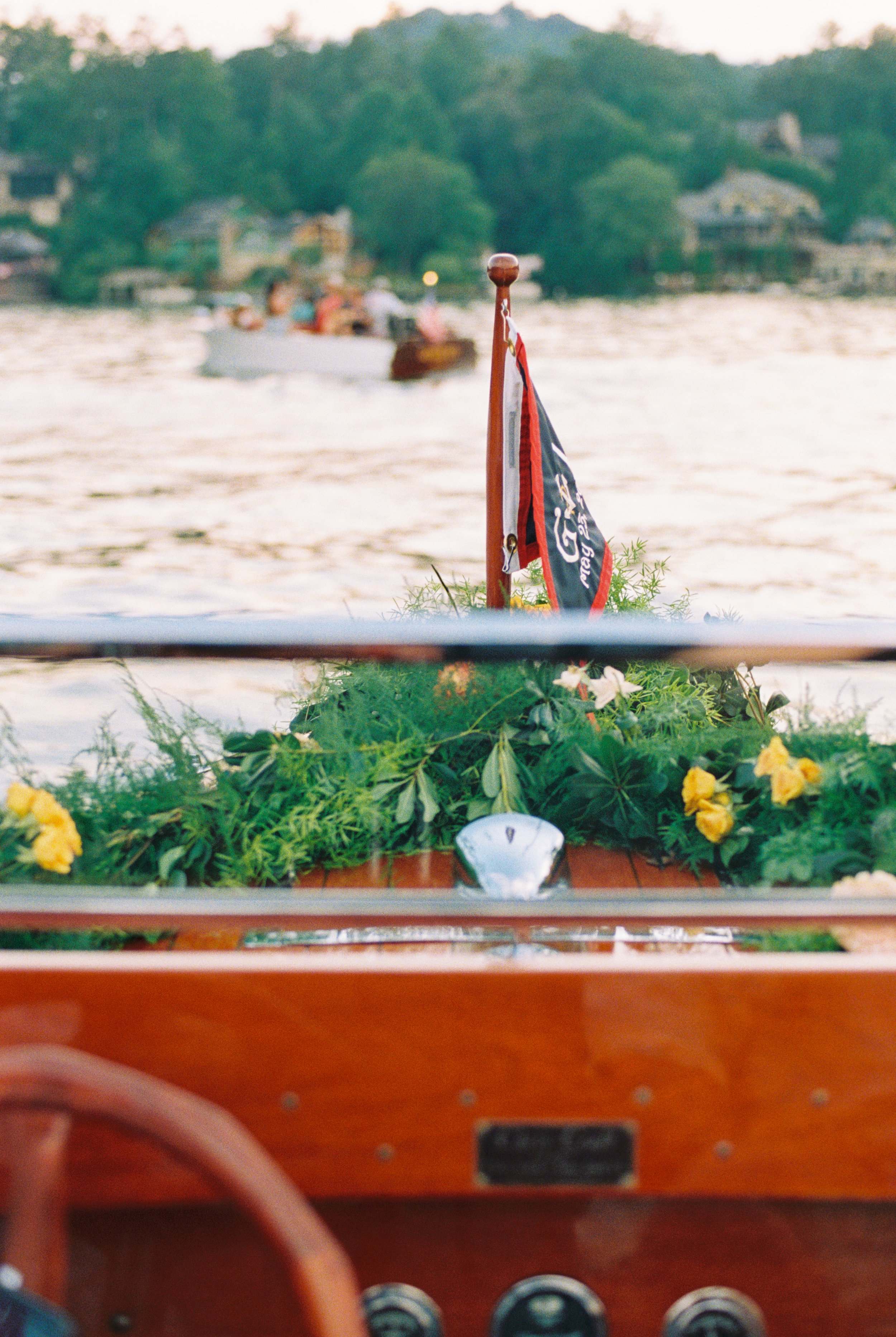 Wooden boat steering wheel with floral decor and flag, boathouse visible across the water