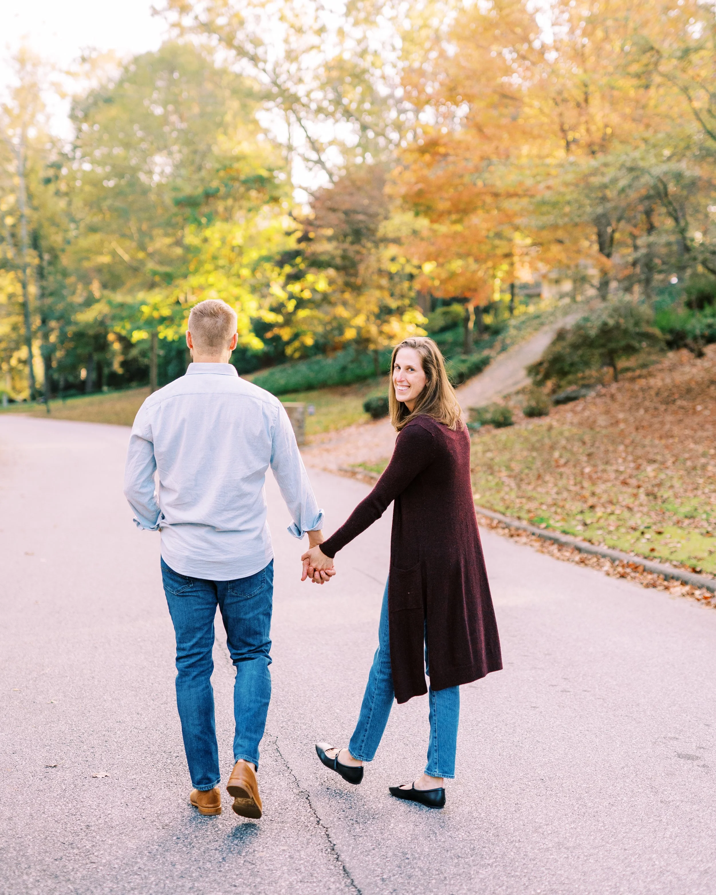 Holly and Chris walking hand in hand along their driveway surrounded by fall foliage in Dunwoody, Georgia