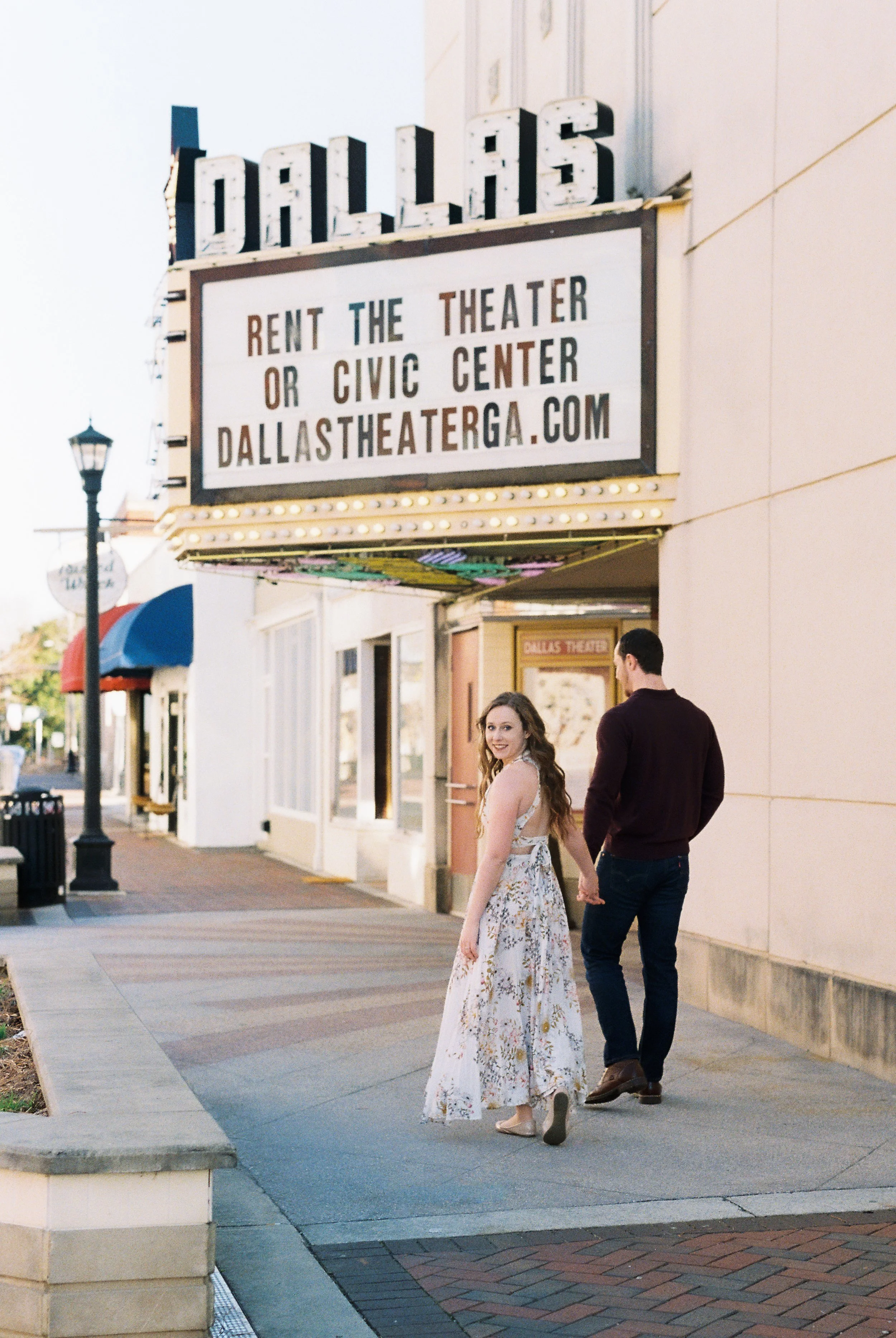 Maddie glances back at the camera while walking hand in hand with Conner past the historic Dallas Theater marquee in Dallas, Georgia.