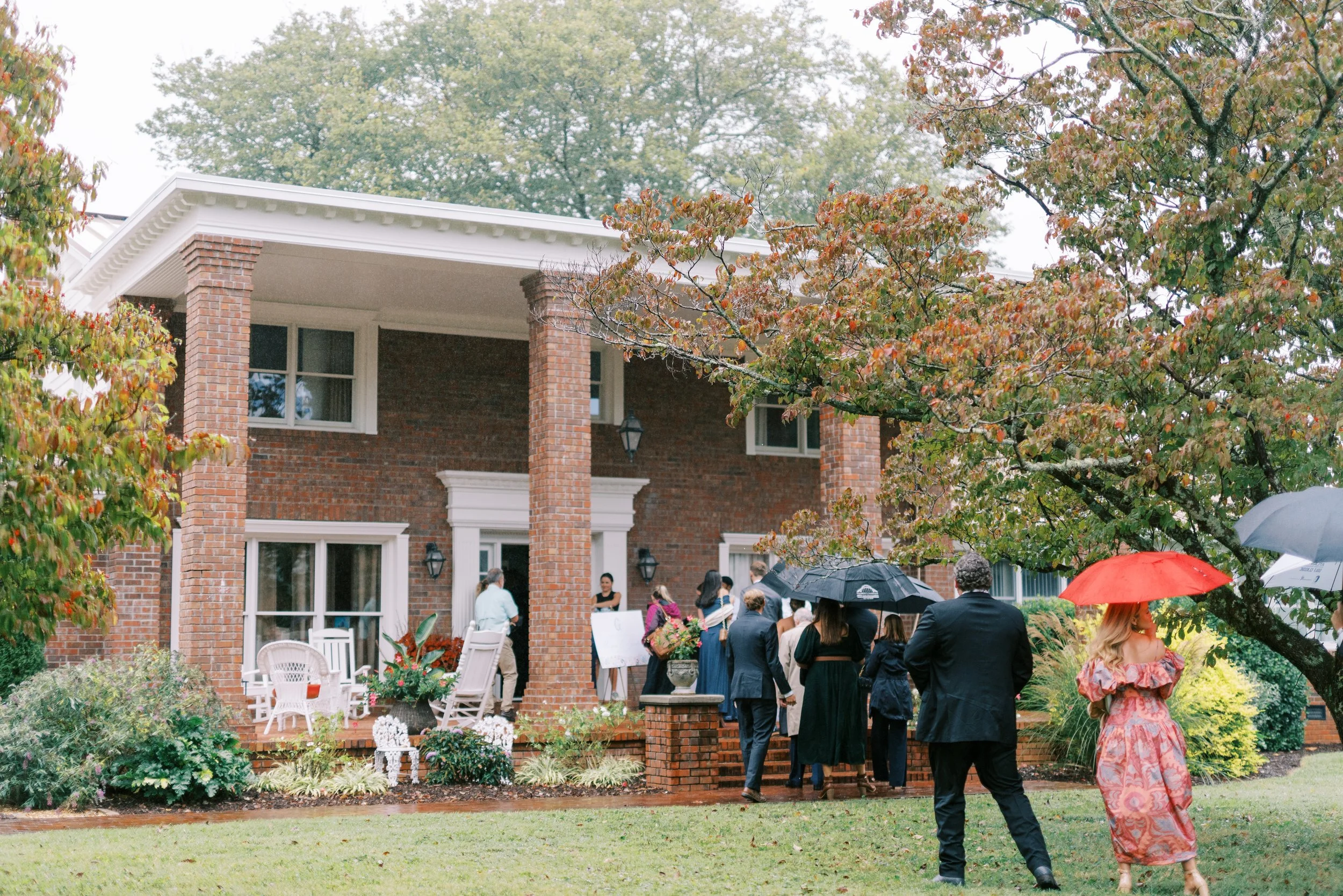 Guests gathering with umbrellas outside the brick venue building