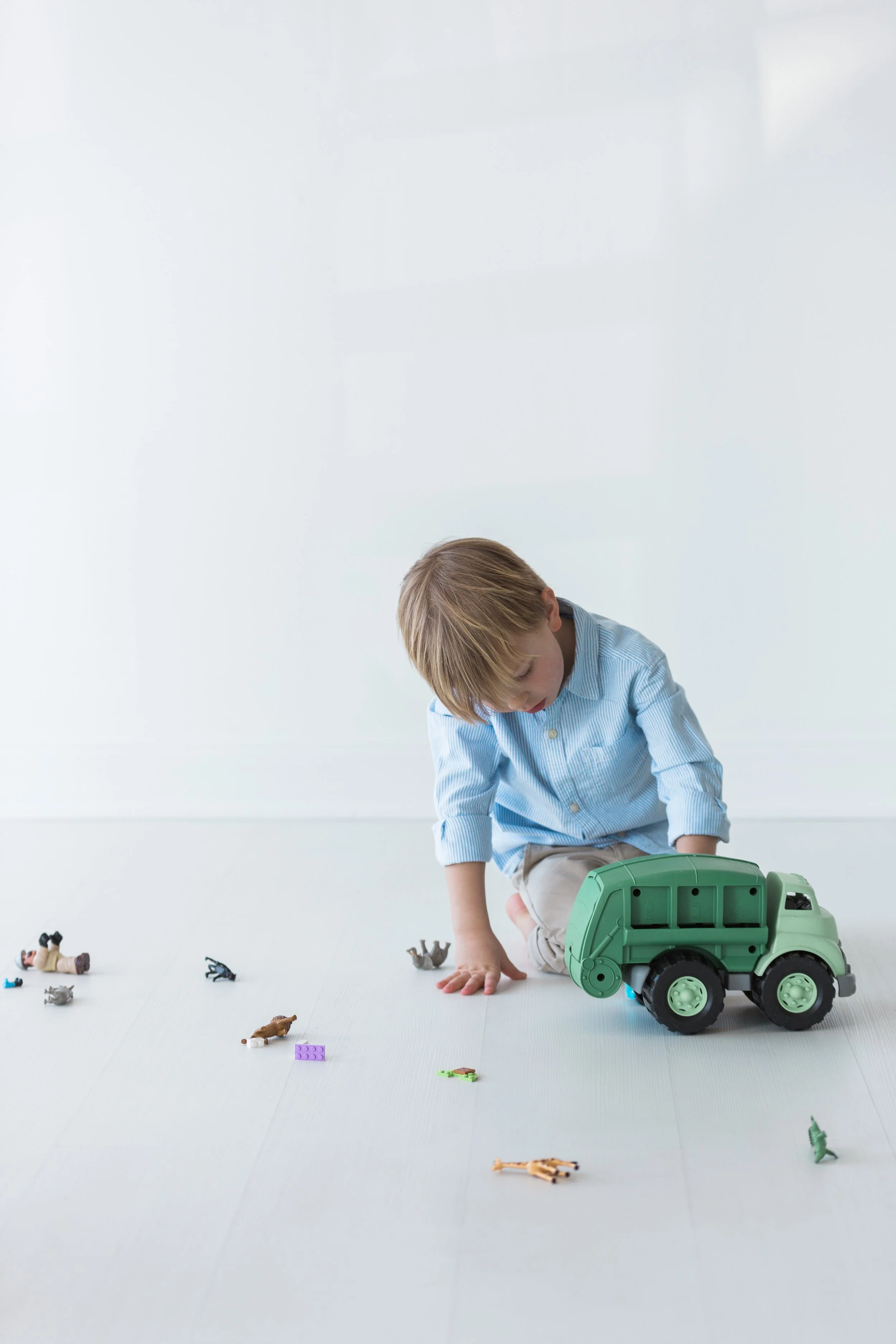 Child playing with toy animals and a toy garbage truck on a white floor.