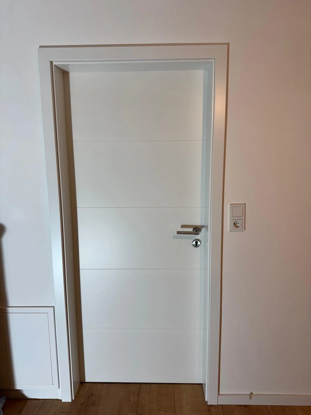 weiße Tür mit horizontalen Linien und moderne Türklinke in einem Raum mit weißem Wand und Holzfußboden
