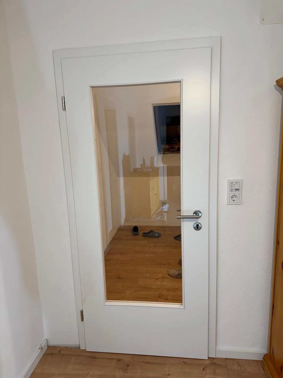 Ein weißer Innenraum mit einer Glastür, die auf einen Flur mit Holzboden führt.