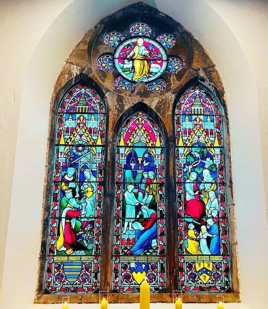 Colorful stained glass windows in St Catherine's  Cultural Centre Kinsale depicting biblical scenes, with a circular window at the top, framed by a stone arch.