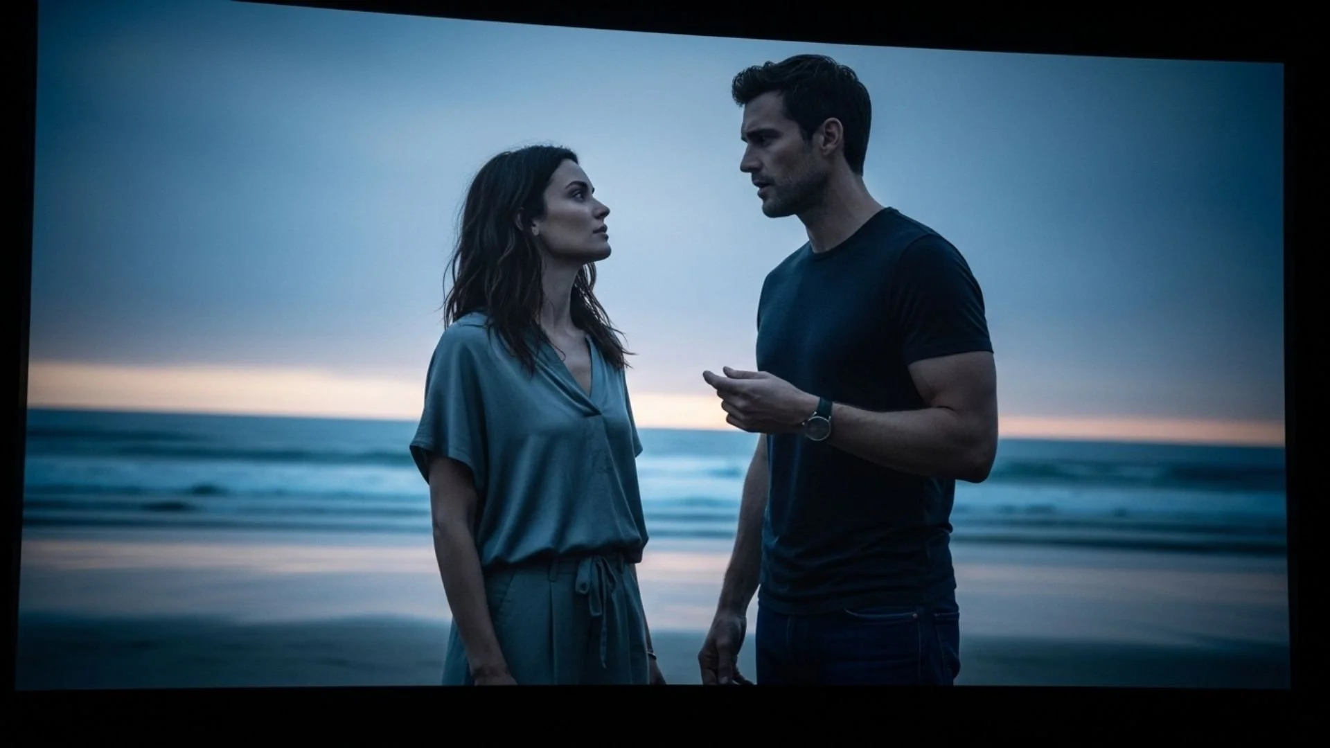 On a movie screen man and a woman stand close together on the beach during dusk, facing each other and engaging in a serious conversation. Movie Nights at St Catherine's Cultural Centre Kinsale.