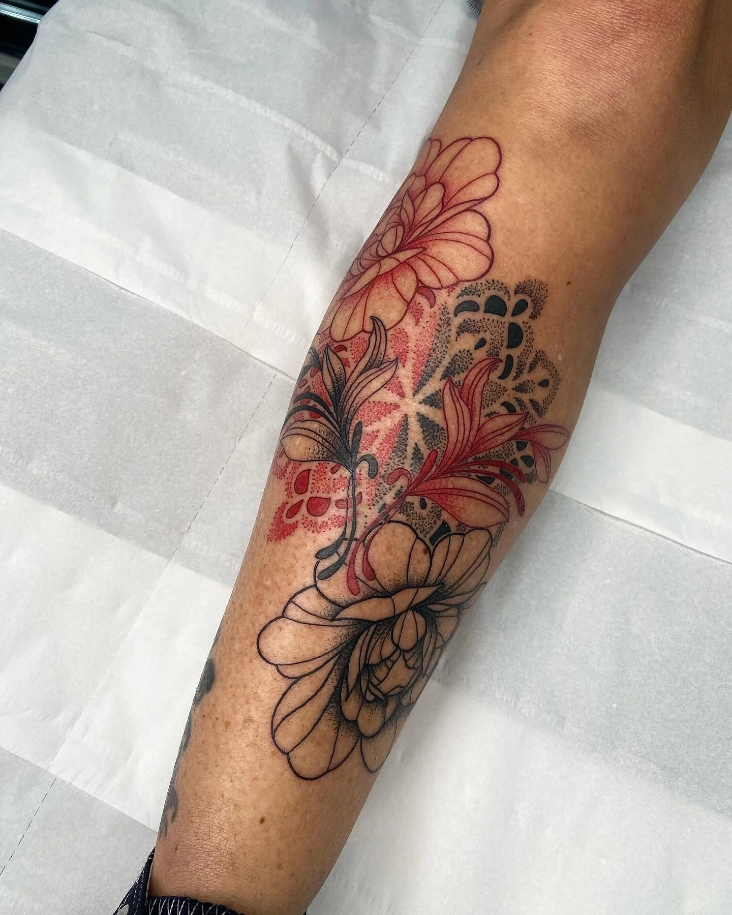 A person's forearm with a tattoo of flowers and butterflies, some parts of the tattoo are being outlined or colored in.