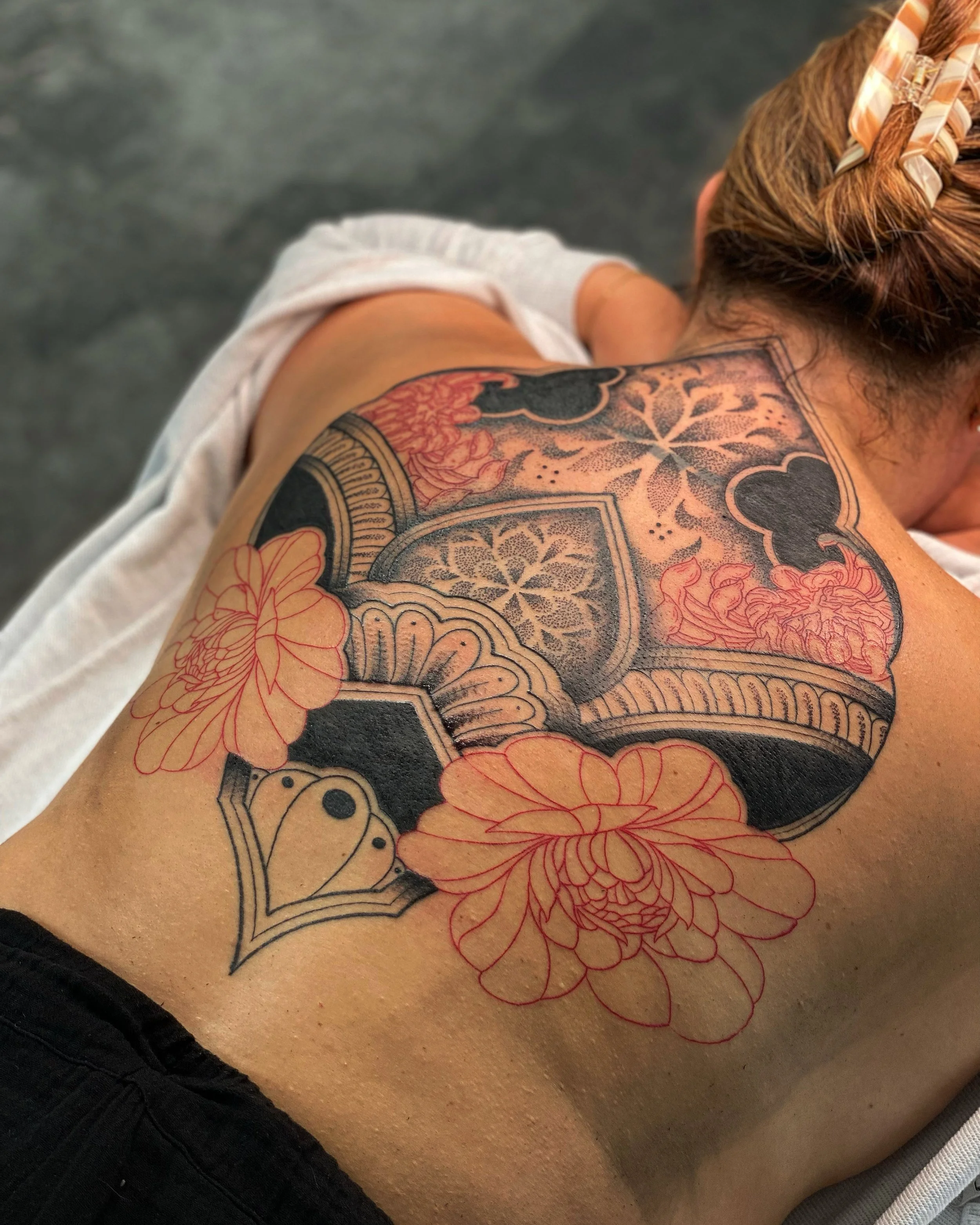 Close-up of a person's shoulder and arm with colorful tattoos, and a portion of their head with red hair styled in braids, wearing a hair clip, lying on a textured surface.