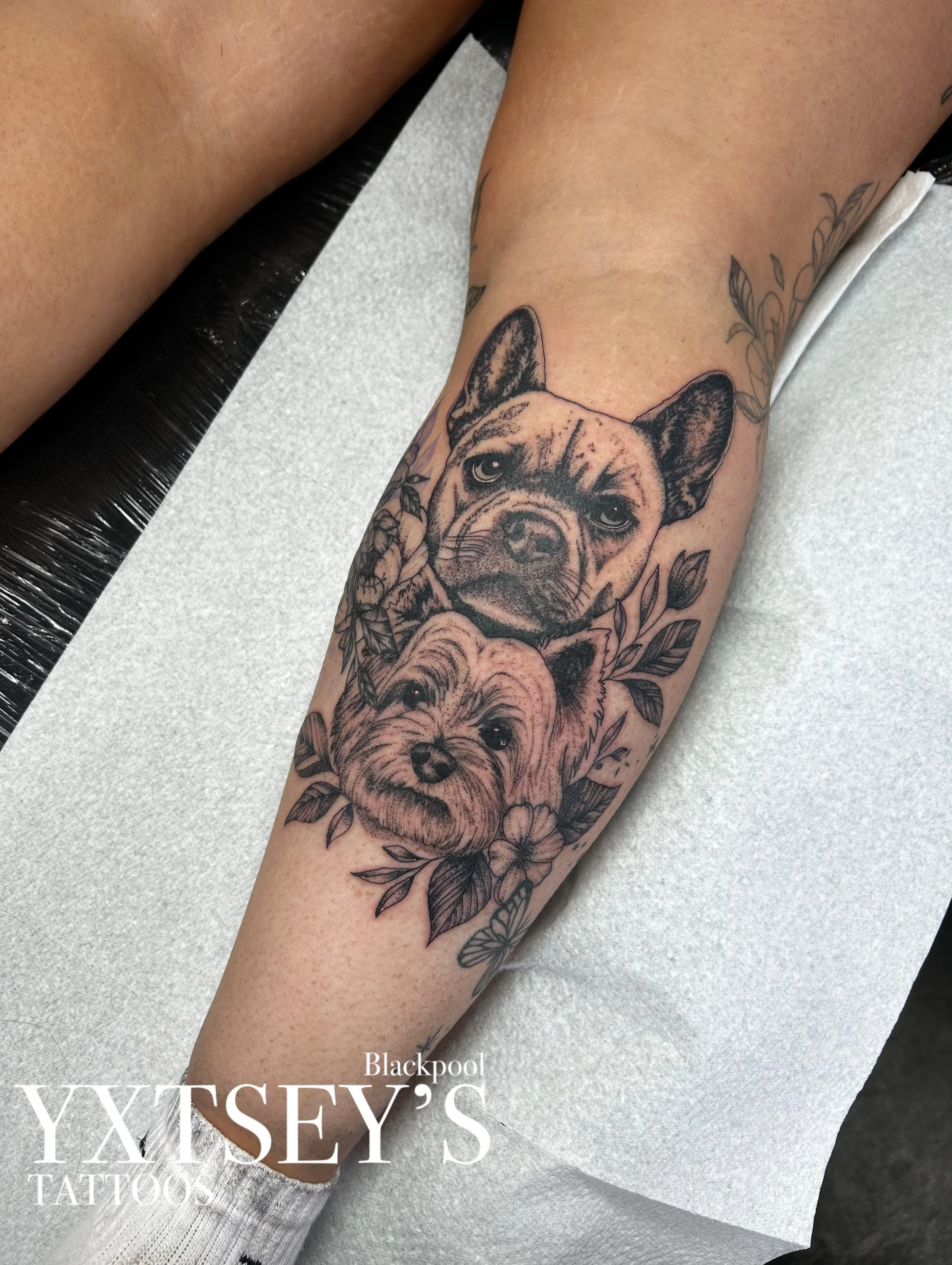 Close-up of a person's forearm with a tattoo of a dog's face surrounded by floral elements.