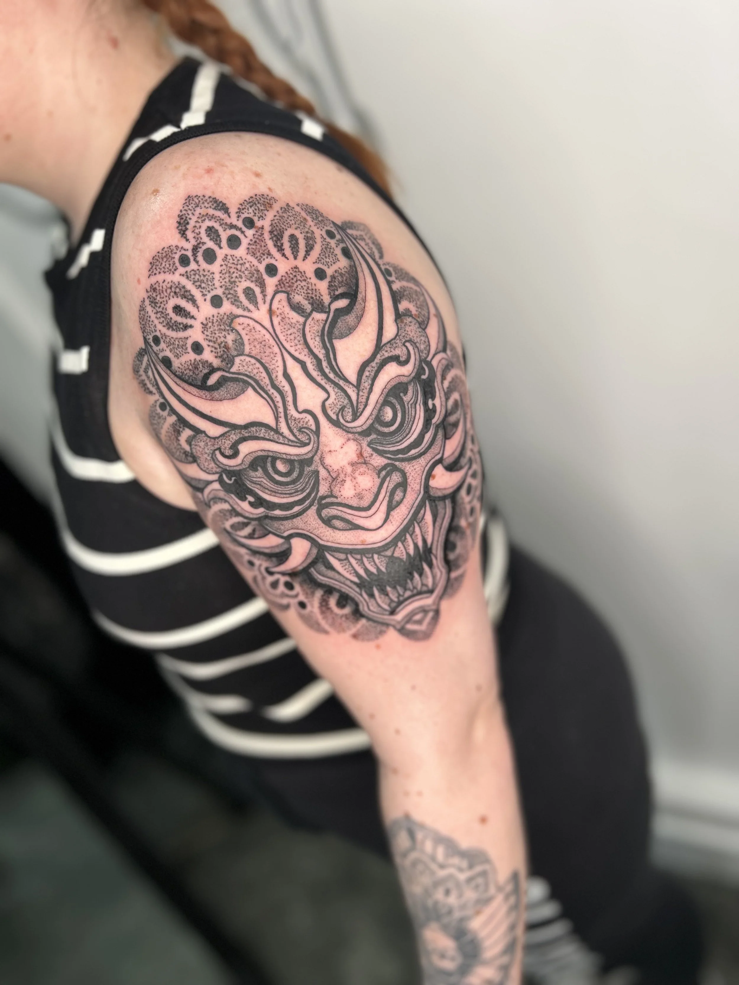 Close-up of a person's upper arm with a detailed black and gray tattoo of a floral skull design.