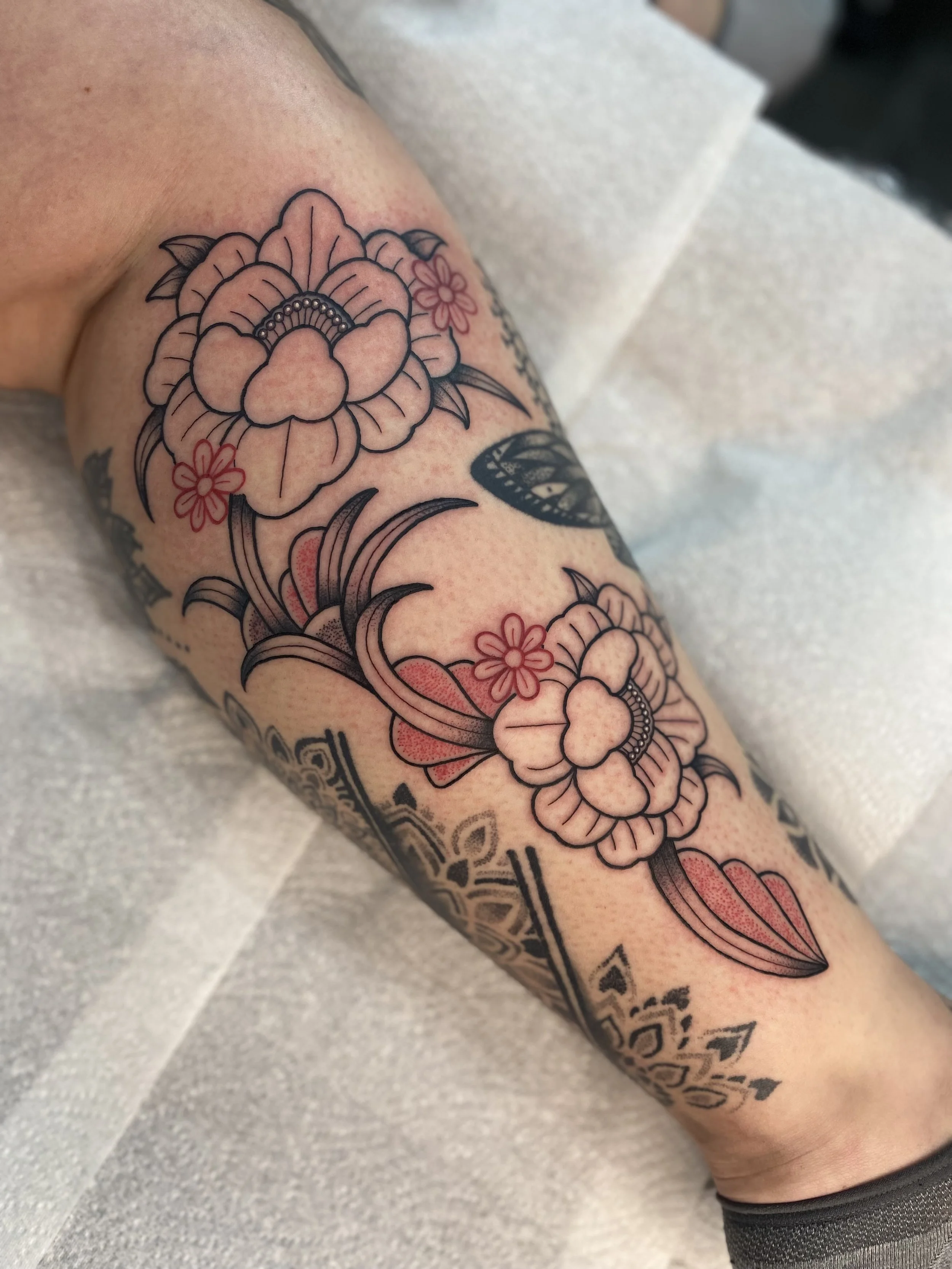 Close-up of a colorful floral tattoo on a person's lower leg, featuring large flowers with detailed petals and leaves.