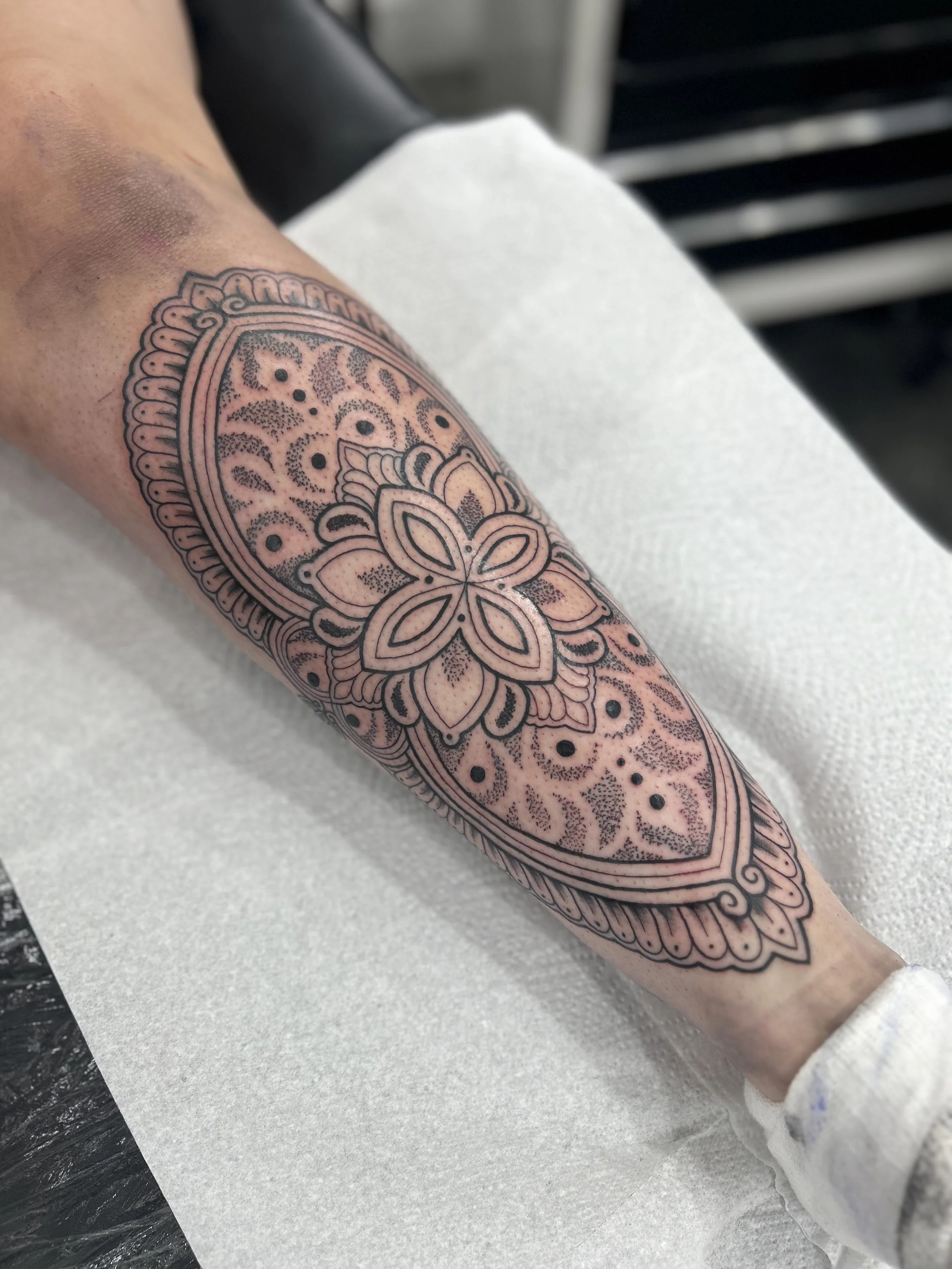 A person's arm with a tattoo featuring an intricate mandala design in black ink.