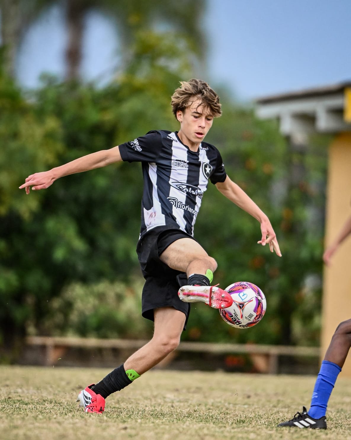 A young male soccer player is kicking a colorful ball during a game, wearing a black and white striped jersey and black shorts.