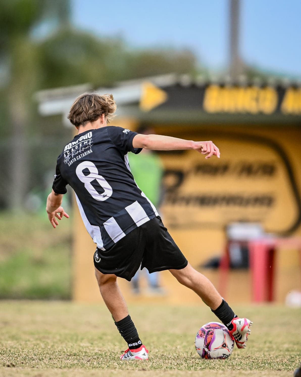 A young male soccer player in a black and white uniform, wearing the number 8, kicks a colorful soccer ball on a grassy field during a game or practice.