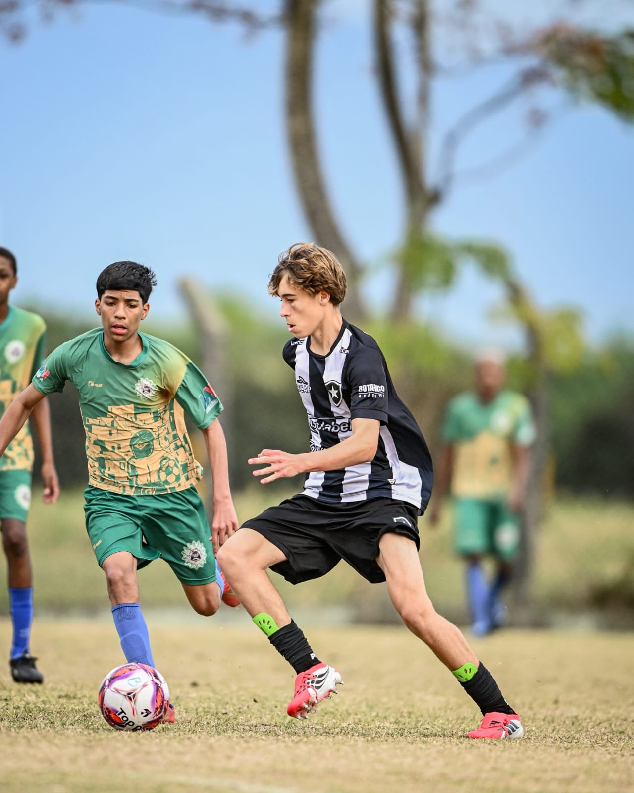 Young soccer players in green and black uniforms competing for the ball on a field.