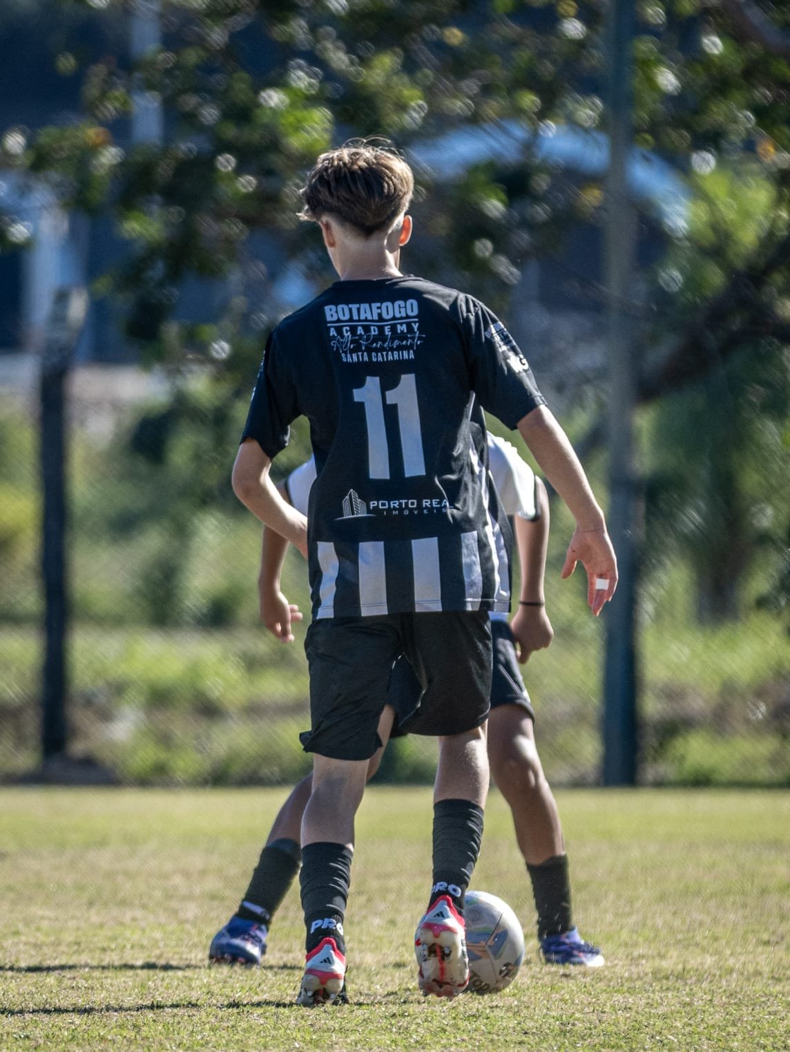 A youth soccer player wearing a black and white striped jersey with the number 11, standing on a soccer field with a ball at their feet, preparing to play.