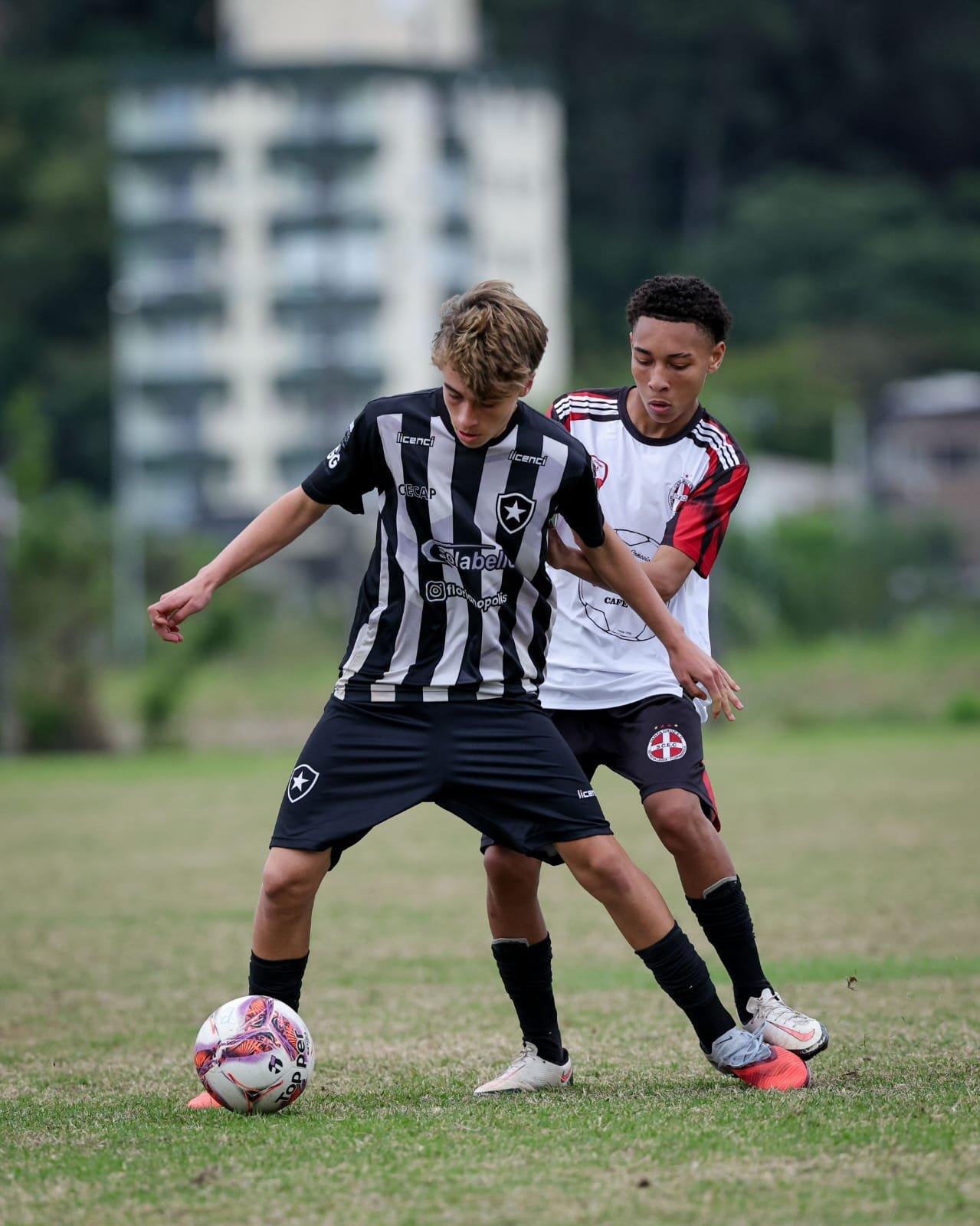 Two young boys playing soccer outdoors on a grassy field, competing for control of the soccer ball.