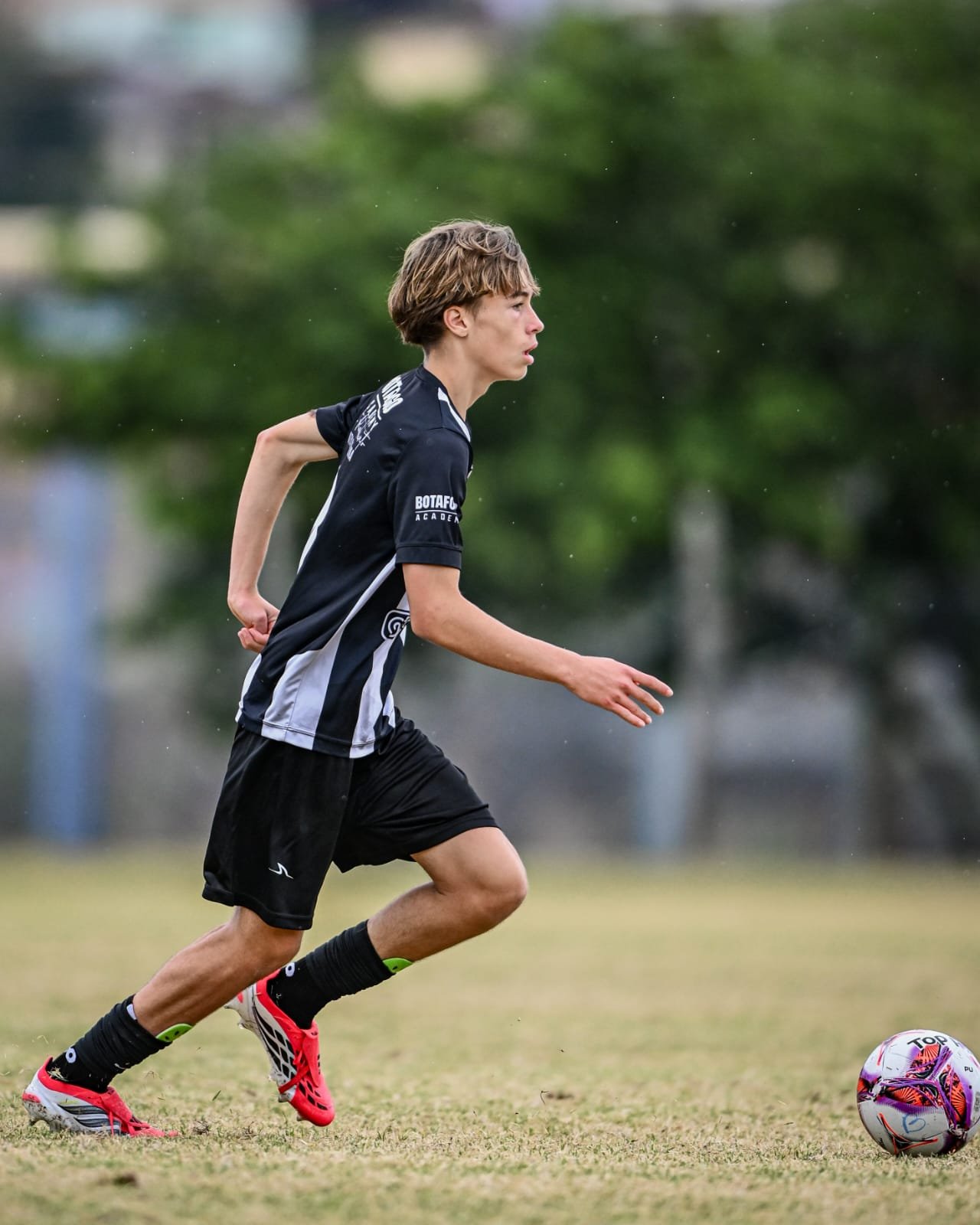A young male soccer player running on a field, wearing a black and white uniform, with a soccer ball nearby.