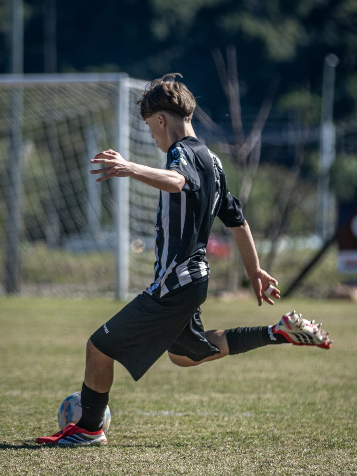 A young male soccer player in black and blue uniform running on a field while controlling the ball with his foot.