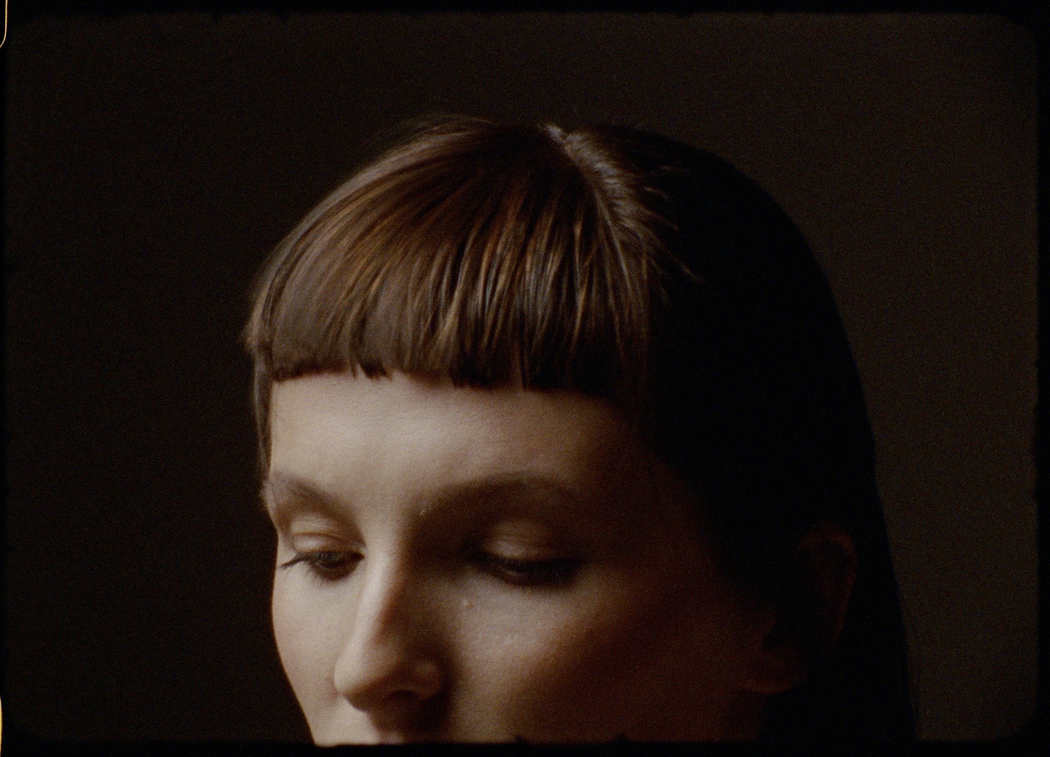 Close-up of a woman with short brown hair, closed eyes, and a dark background.