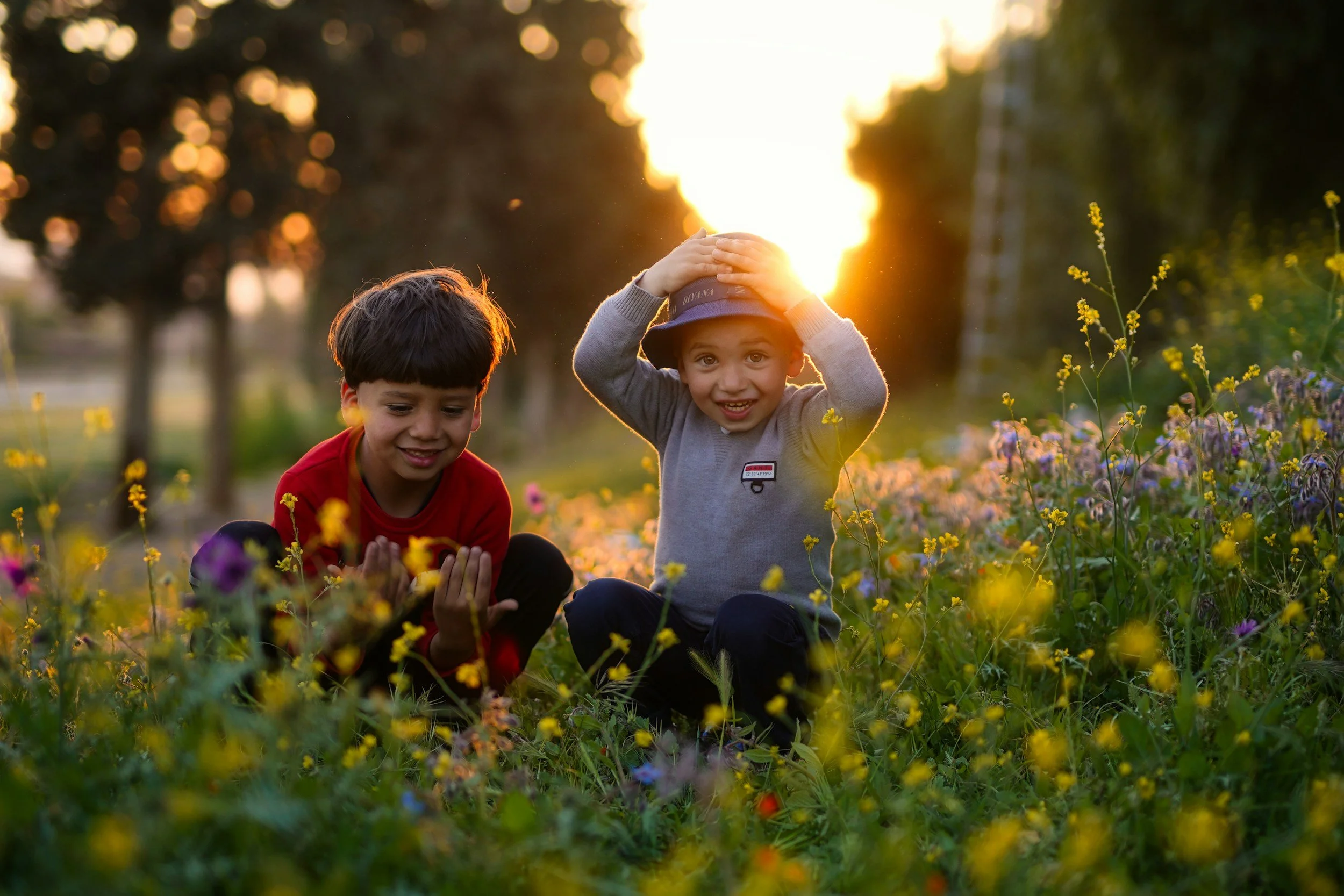 Two young boys sitting in a field of colorful flowers at sunset, smiling and enjoying the outdoors.