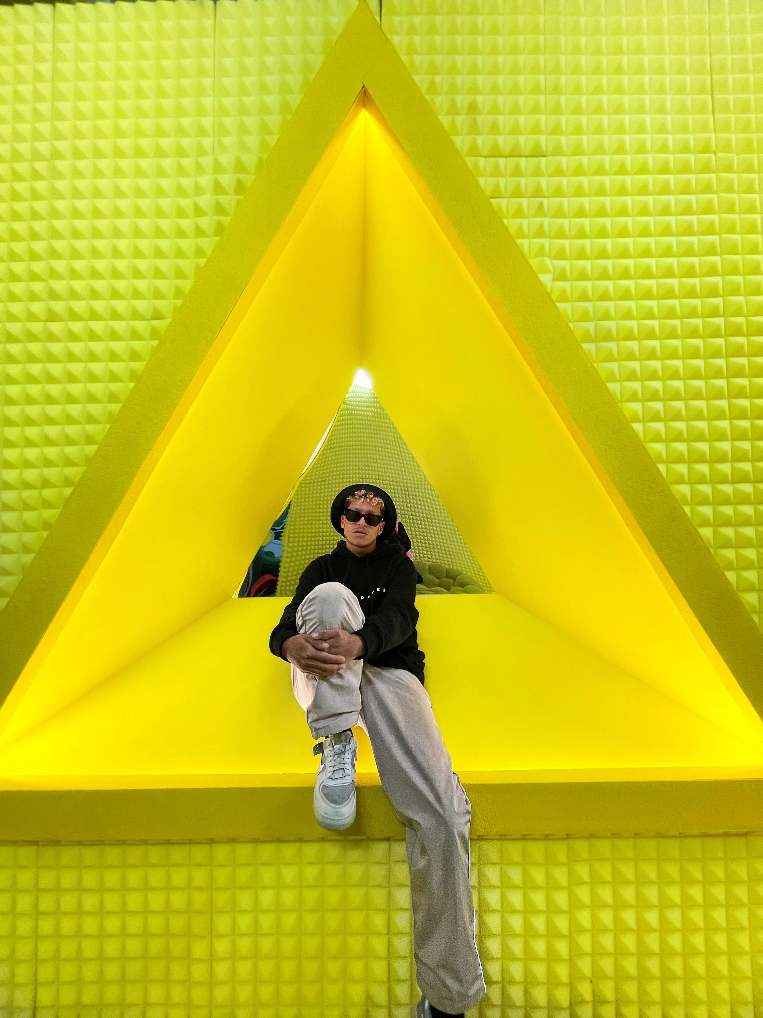 Jeune homme assis dans une structure colorée jaune avec un design géométrique en forme de triangle.