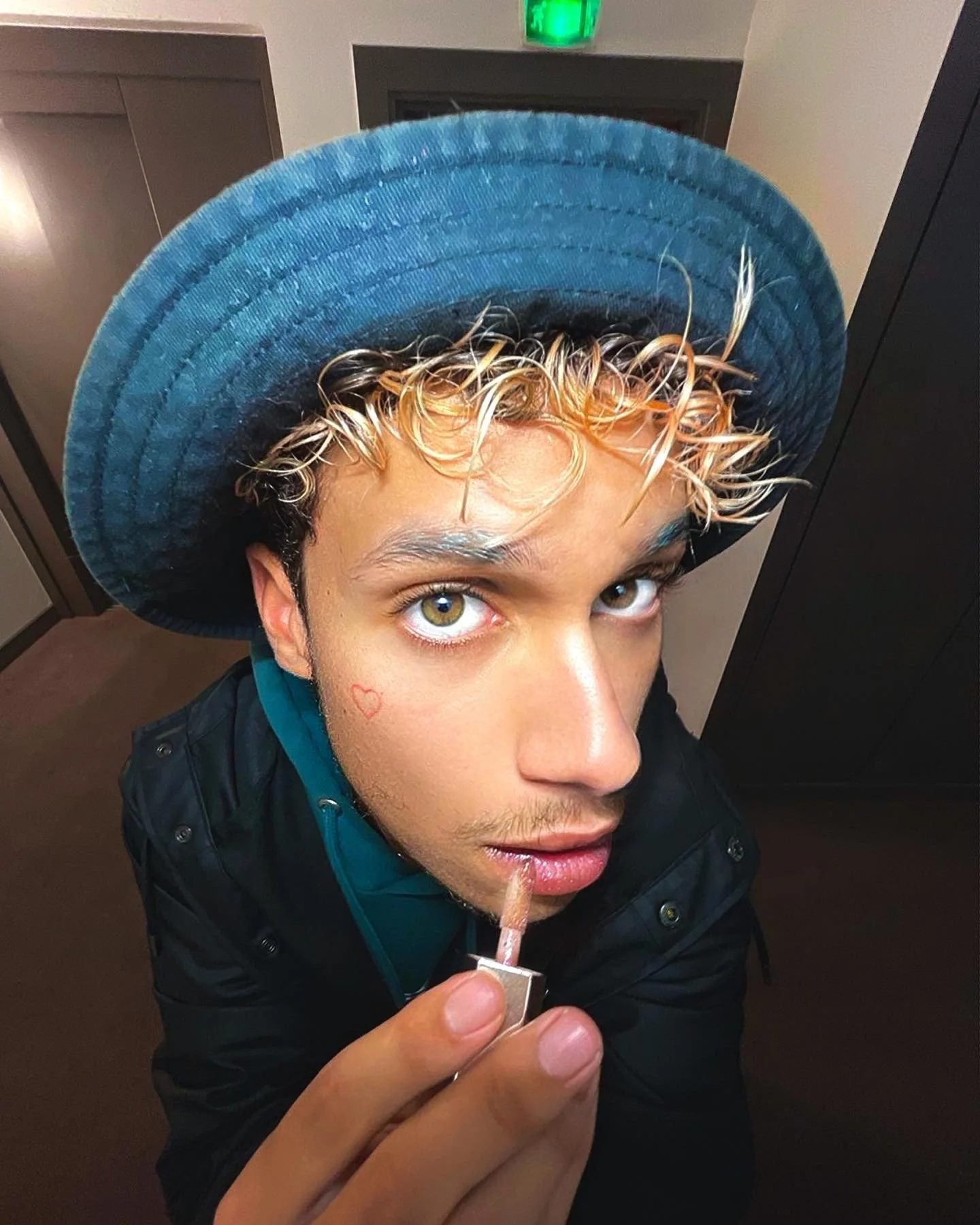 Une personne portant un chapeau bleu applique du maquillage sur ses lèvres.