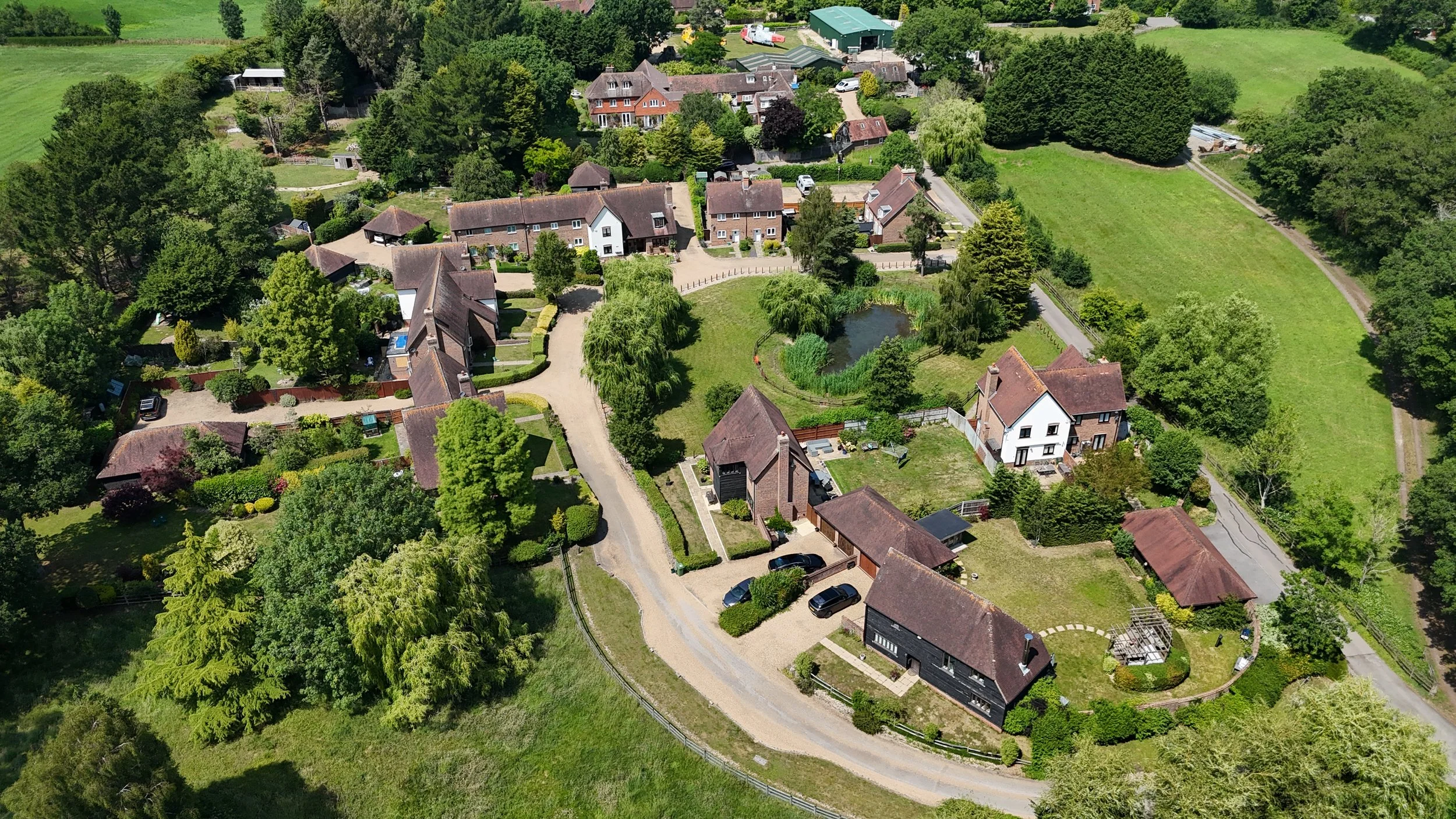 Aerial view of a residential neighborhood with houses, lush green trees, a pond, and well-maintained lawns.