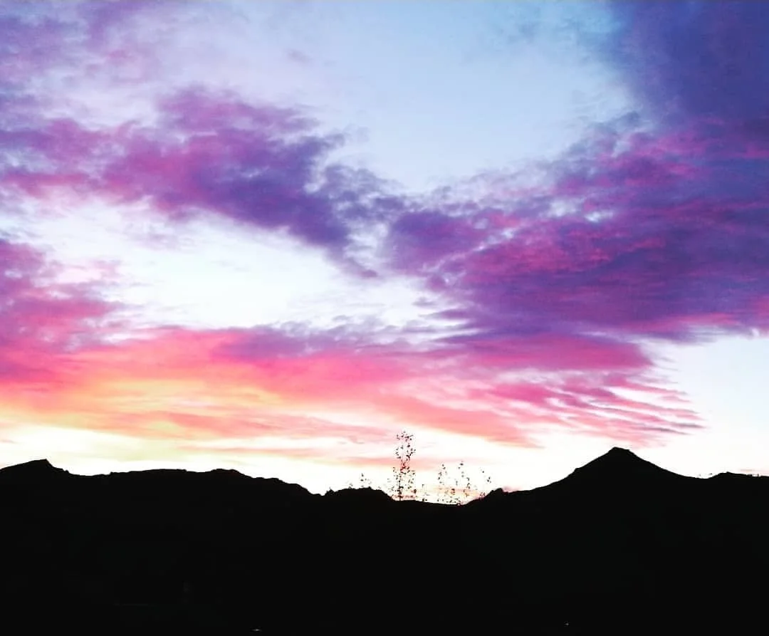 Colorful sunset sky with shades of pink, purple, and blue over a silhouette of mountain range.
