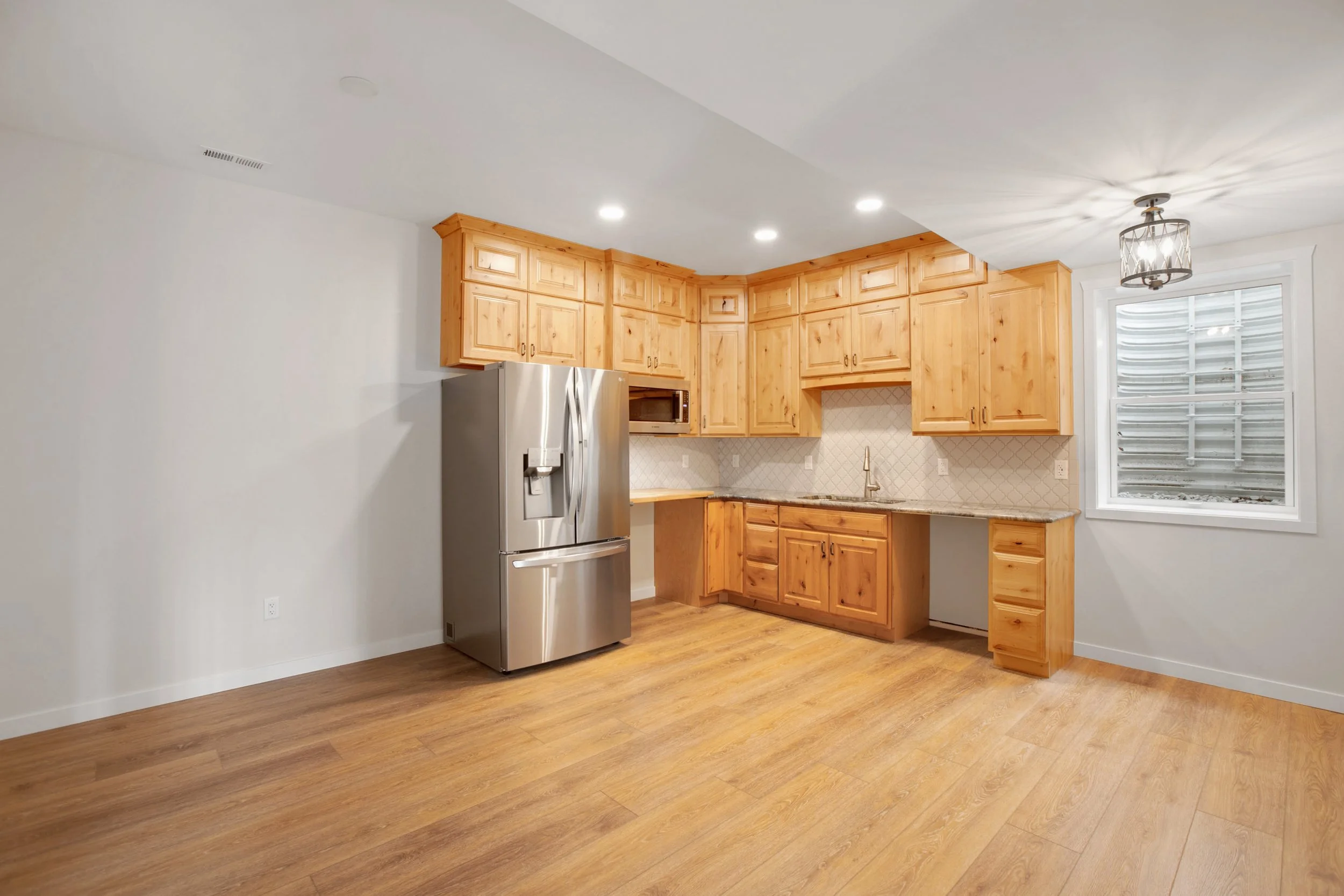 Kitchen with light wood cabinets, stainless steel refrigerator, and wood flooring.