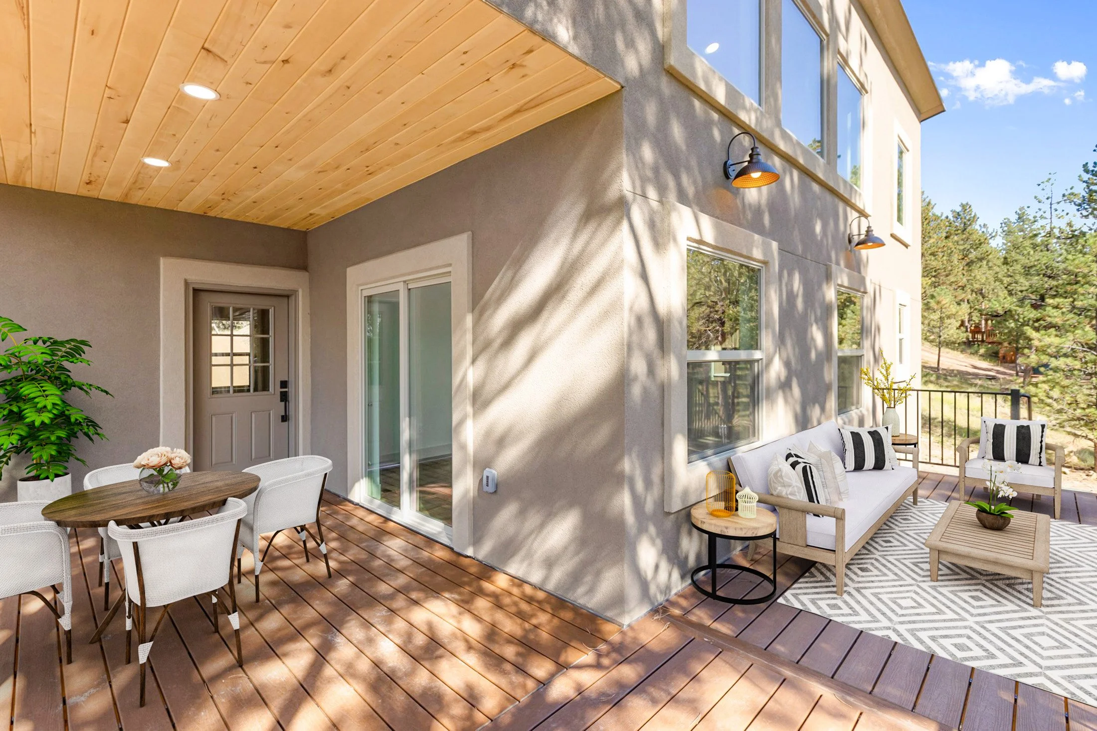 Outdoor patio area with wooden flooring, white outdoor furniture with black and white cushions, a dining table with white chairs, potted plants, and a view of trees and a blue sky.