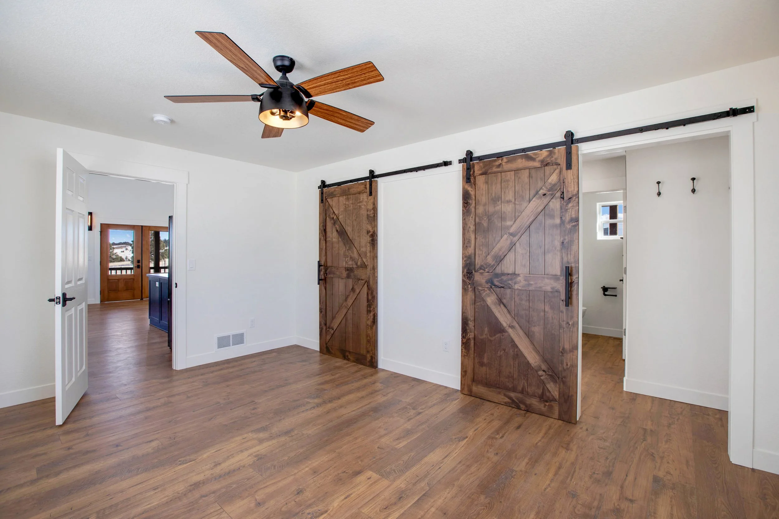 Interior of a house with hardwood floors, white walls, ceiling fan with wooden blades, and sliding barn doors on a track.