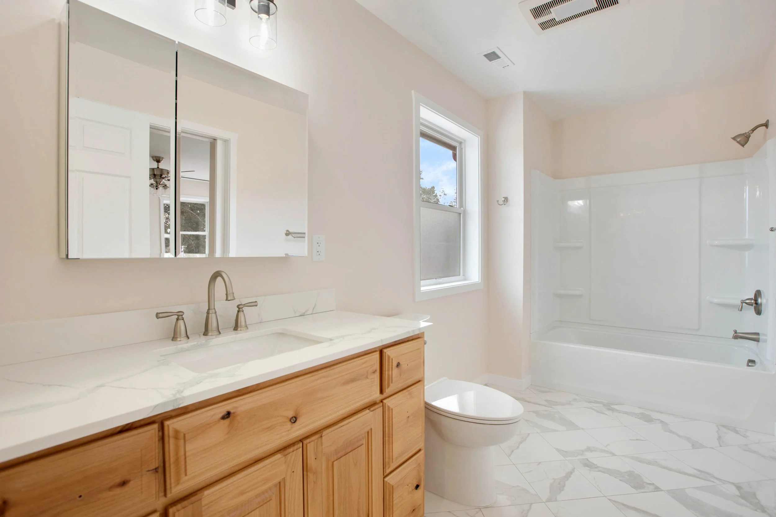 Modern bathroom with white walls, a wooden vanity with a marble countertop, a mirror, a window, and a shower with white walls and chrome fixtures.