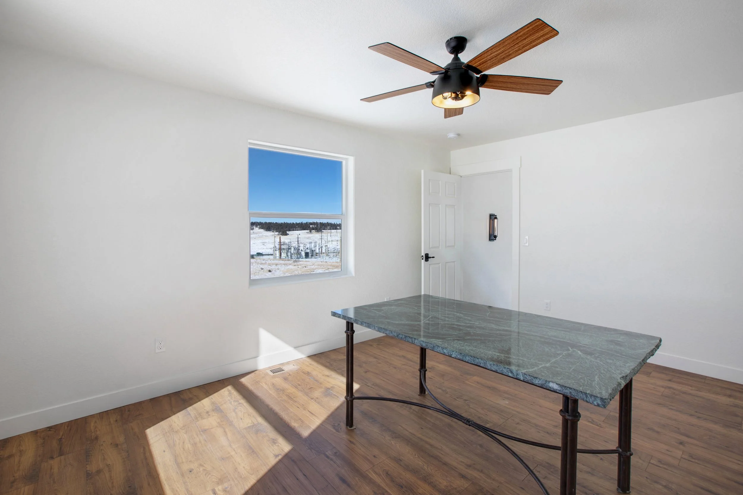 Empty room with white walls, a window showing a snowy landscape, a ceiling fan, and a table with a marble top and metal legs.