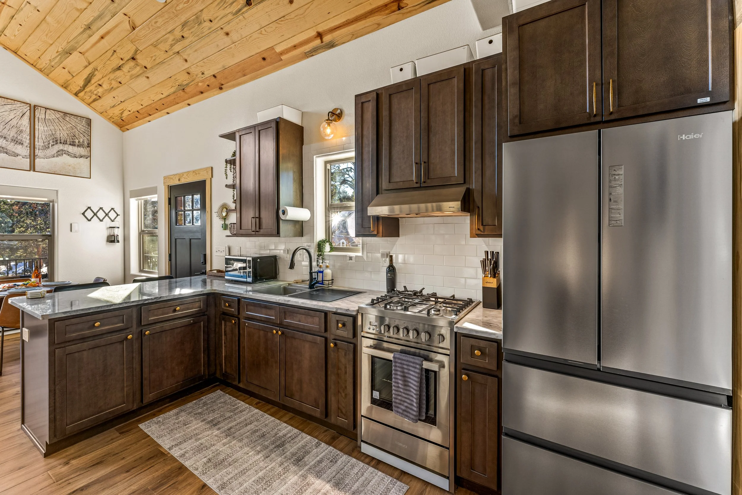 Kitchen with dark wood cabinets, stainless steel refrigerator, and stove, with white subway tile backsplash and windows letting in natural light.