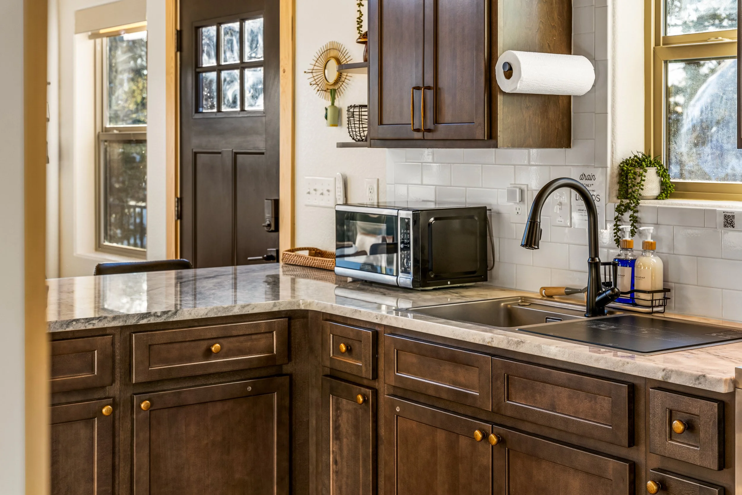 Kitchen with dark wood cabinets, a granite countertop, a microwave, a paper towel roll, and a window with a plant on the windowsill.