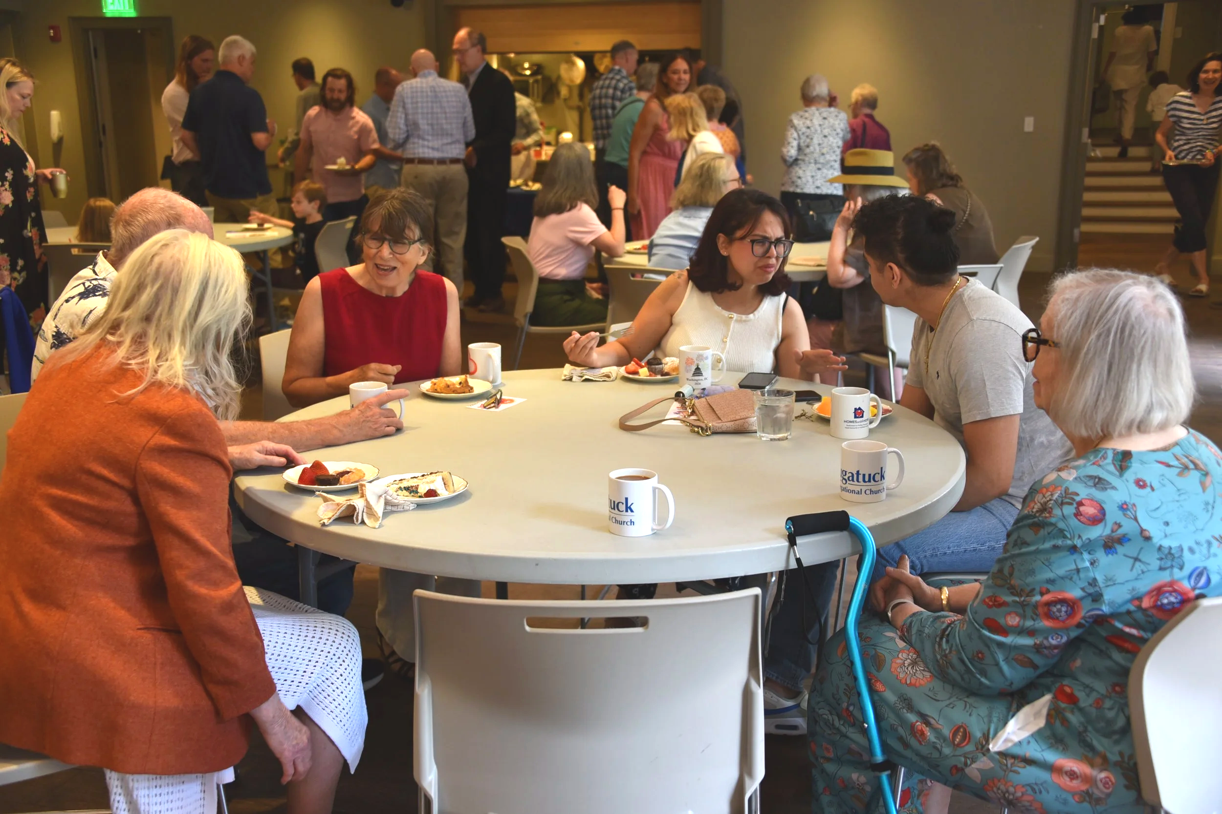 People gathered around a table at a social event, enjoying food and conversations indoors.