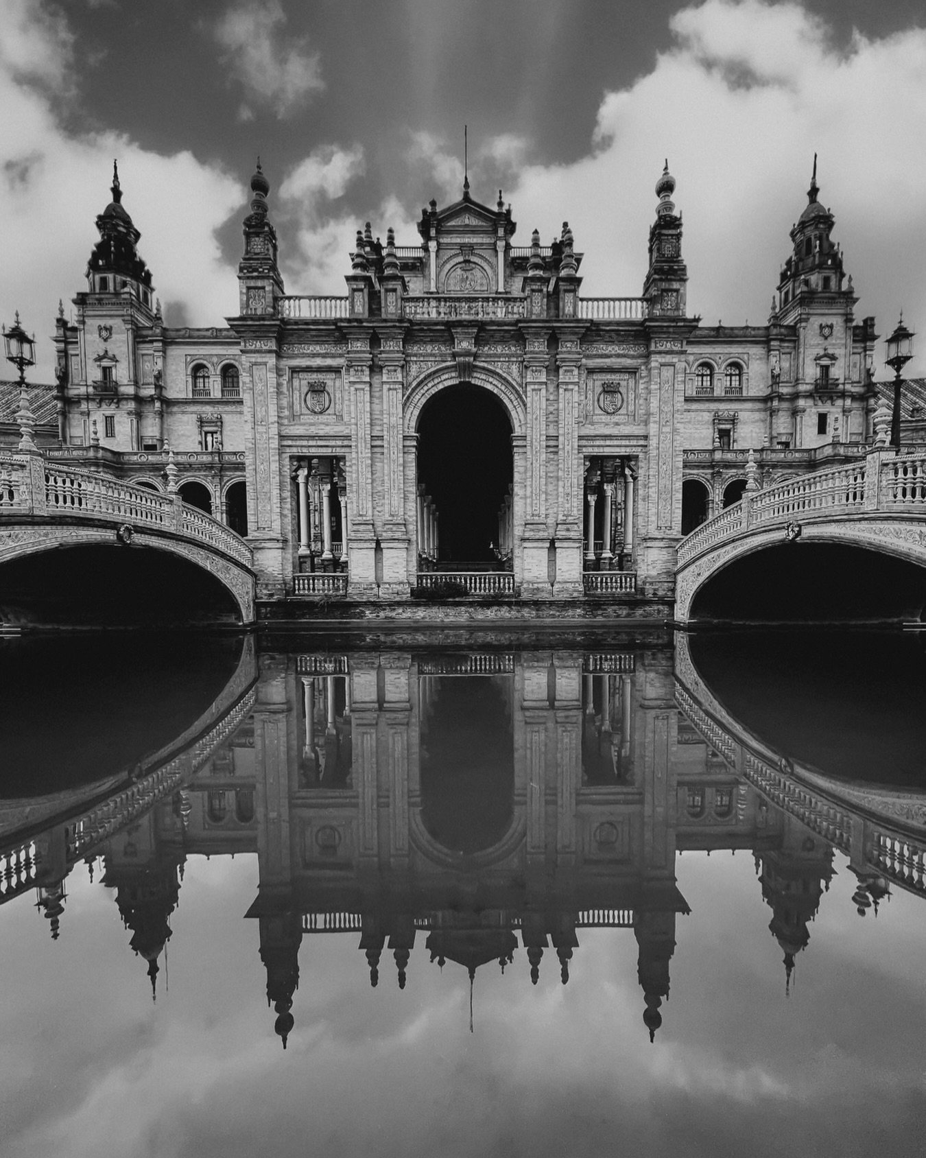 Plaza De Espa&ntilde;a .
Reflections of Plaza de Espa&ntilde;a in Sevilla capture a timeless symmetry, where ornate arches, rising towers, and soft clouds merge in still water. The black-and-white tones highlight every detail, turning the scene into 