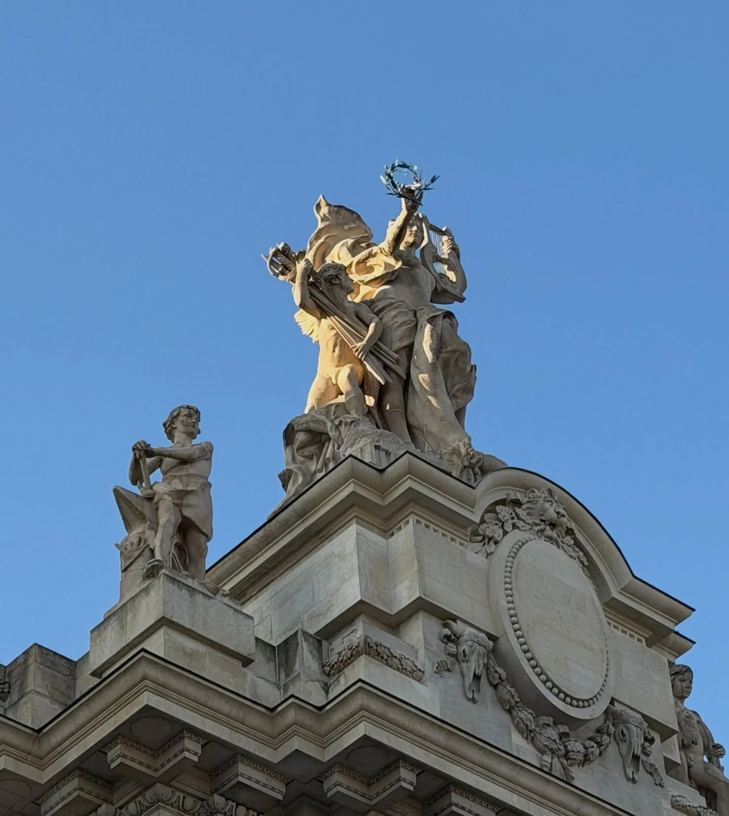 Looking up at the Grand Palais in Paris, sculpted stone figures crown the skyline with timeless grace. Against a flawless blue sky, classical allegory, movement, and craftsmanship converge, reminding us how architecture, art, and history merge into a