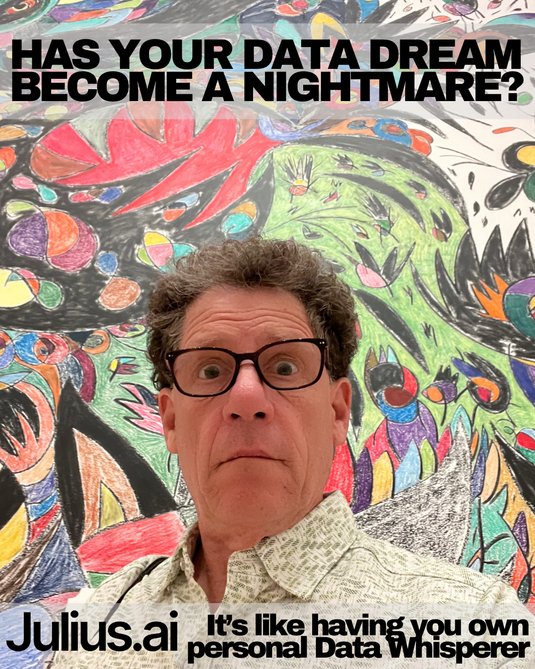 A man with glasses posing in front of a colorful, abstract, chalk or crayon drawing on a wall.