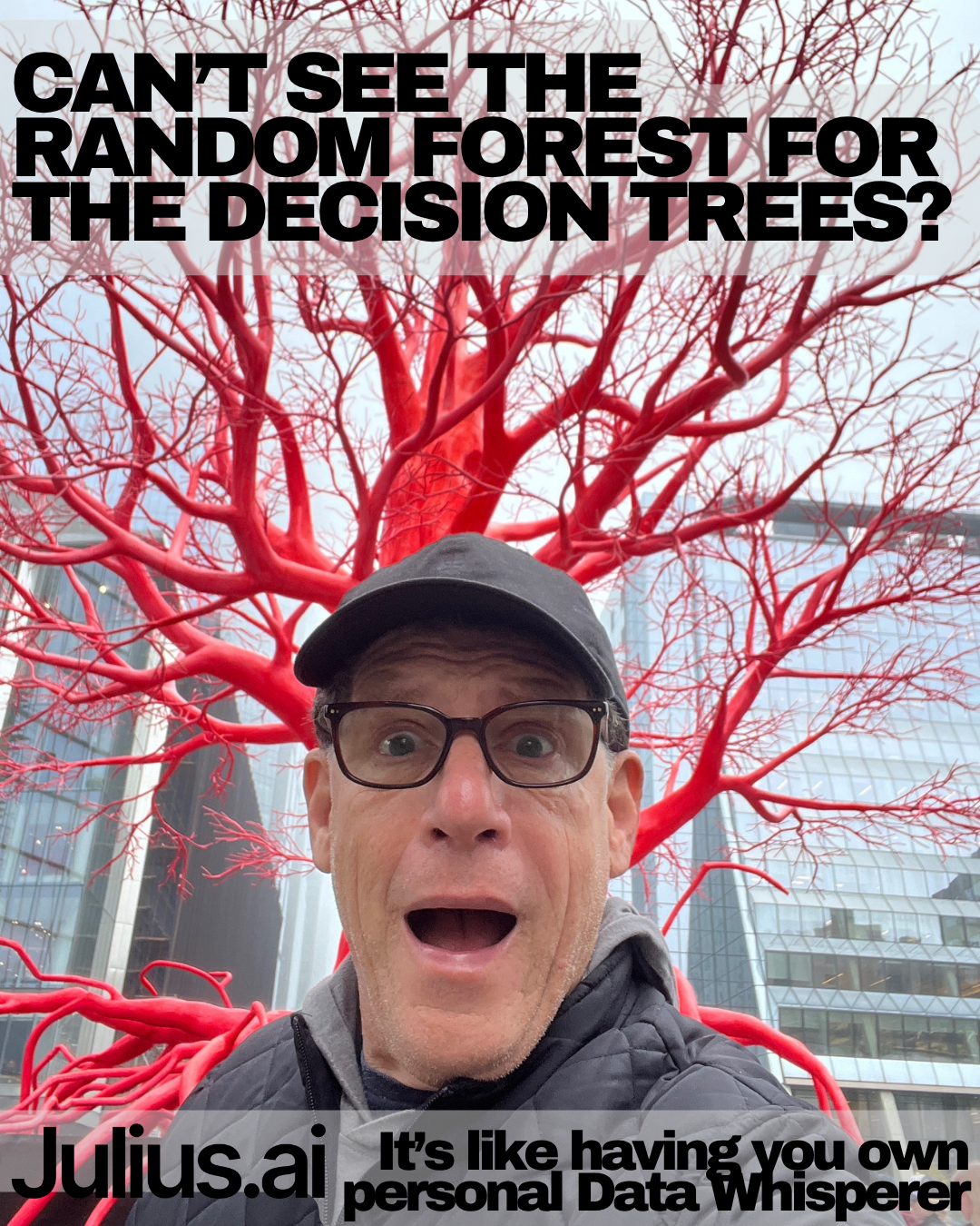 A man taking a selfie next to a red, leafless tree sculpture in an urban area with glass buildings in the background.