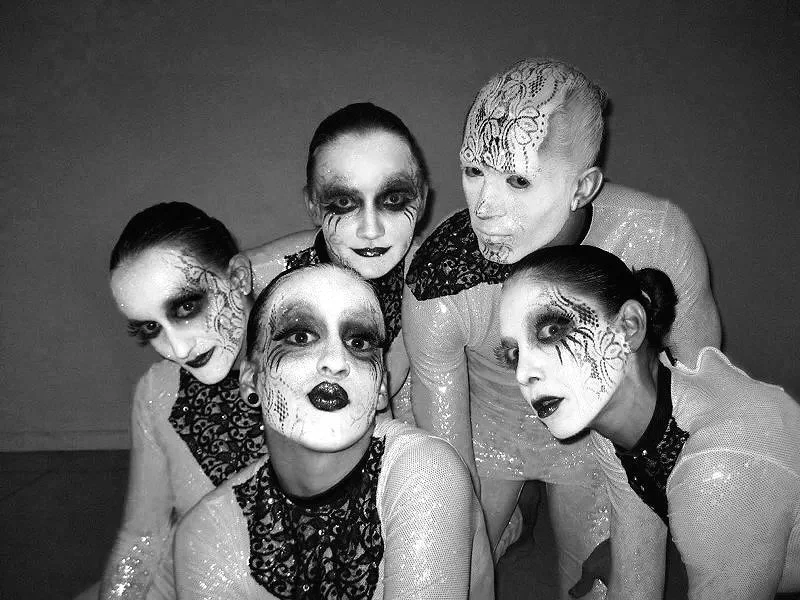 Group of five dancers with face paint and costumes, posing together in black and white.