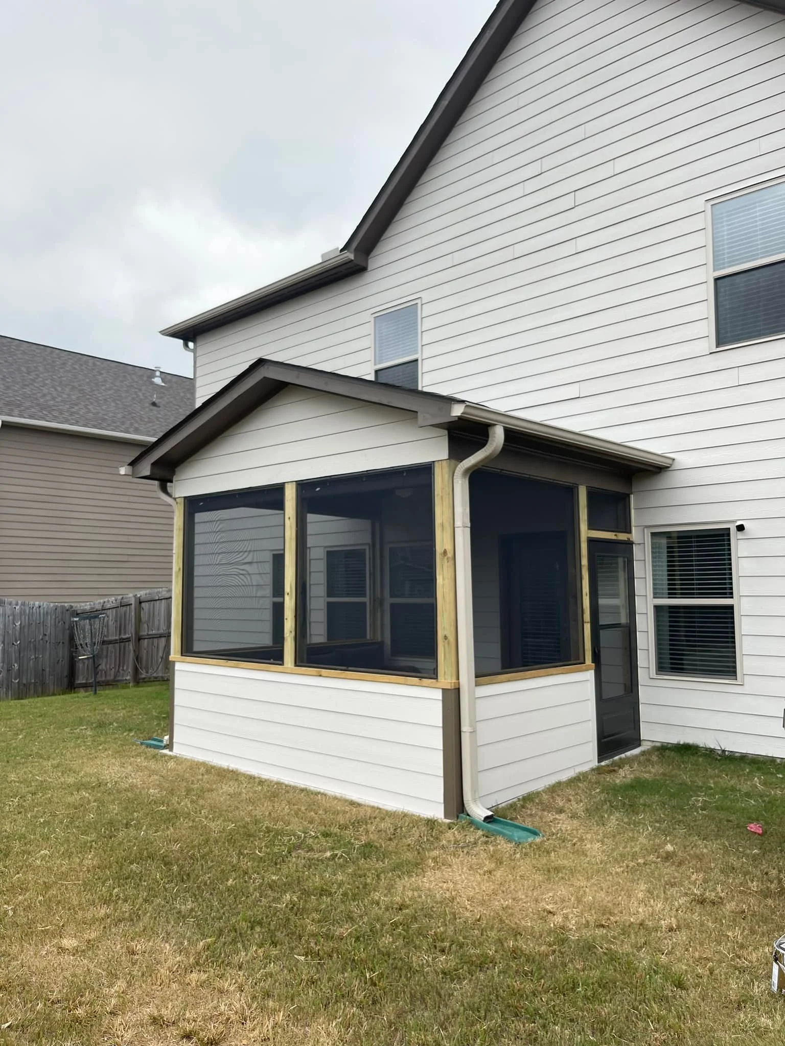 Backyard with a white house and a newly built screened porch with black framing.