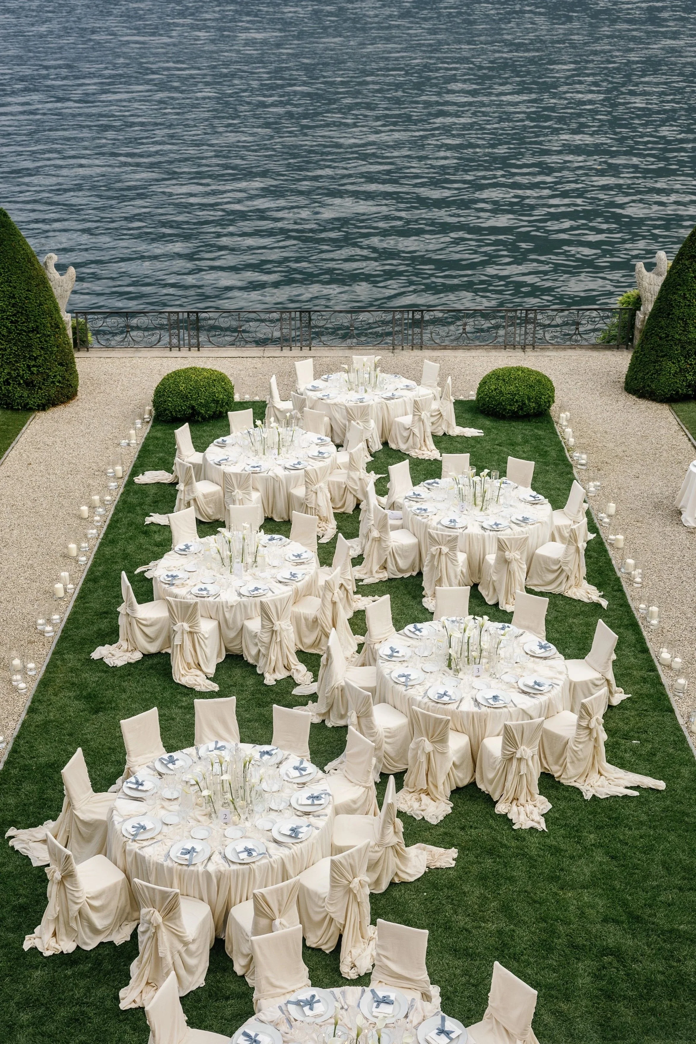An intimate lakefront wedding dinner at Villa Balbiano, Lake Como, styled with fully draped round tables and chairs, sculptural fabric details, framed by the iconic waters of the lake.