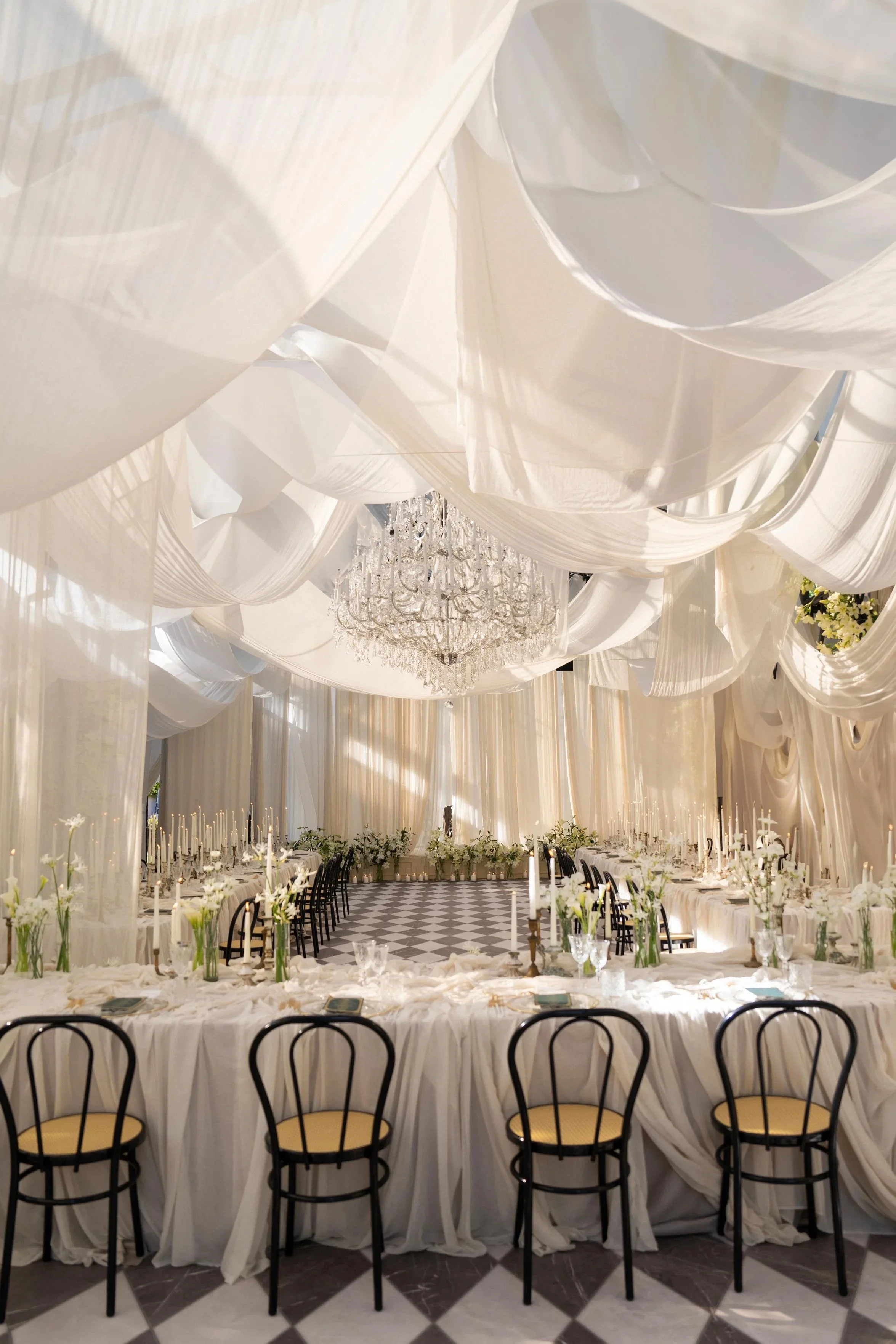 An airy glasshouse reception at Villa Balbiano, Lake Como, layered with flowing white drapery and a crystal chandelier, where vintage 1920s elegance meets the rock’n’roll spirit of the couple.