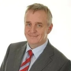 Portrait of a middle-aged man in a gray suit, white shirt, and red-striped tie, smiling against a plain white background.