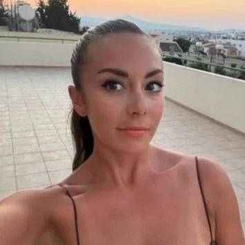 A woman taking a selfie on a rooftop with a city skyline in the background.