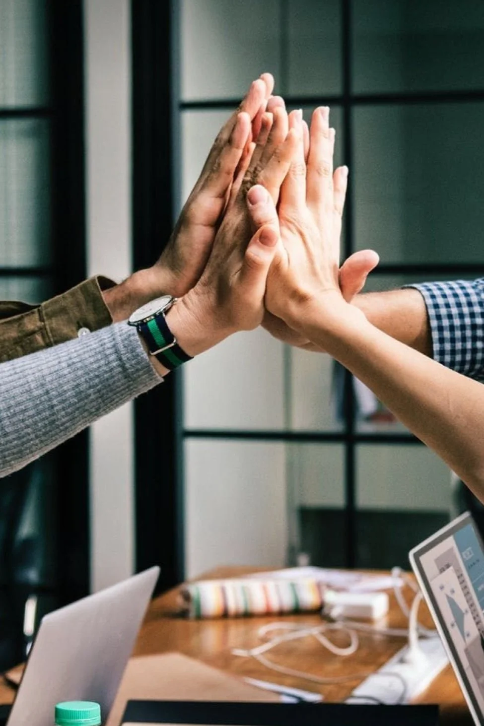 Group of hands high-fiving in an office setting.