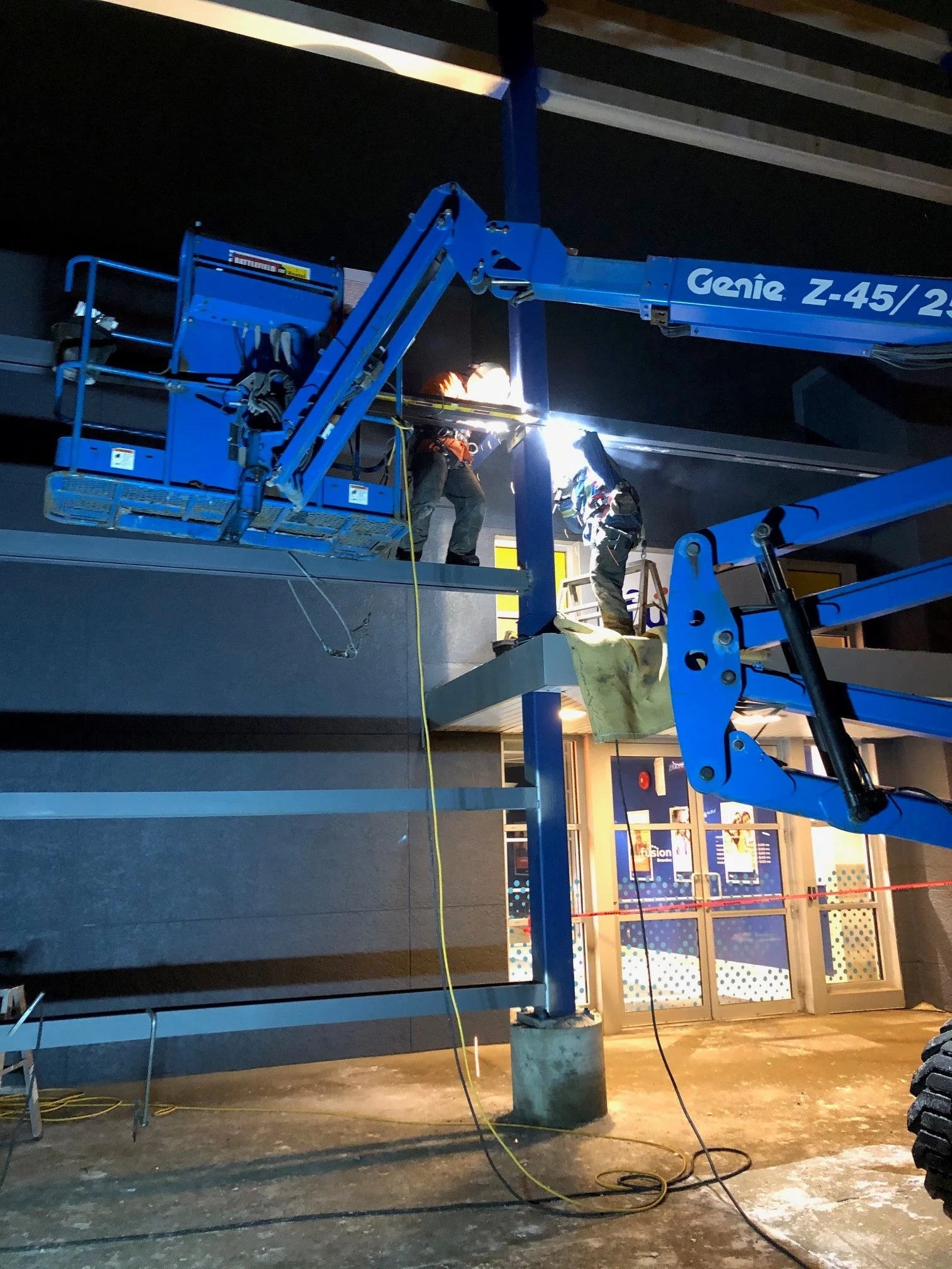 Workers welding on the top floor of a building using a blue lift in an indoor construction or renovation setting at night