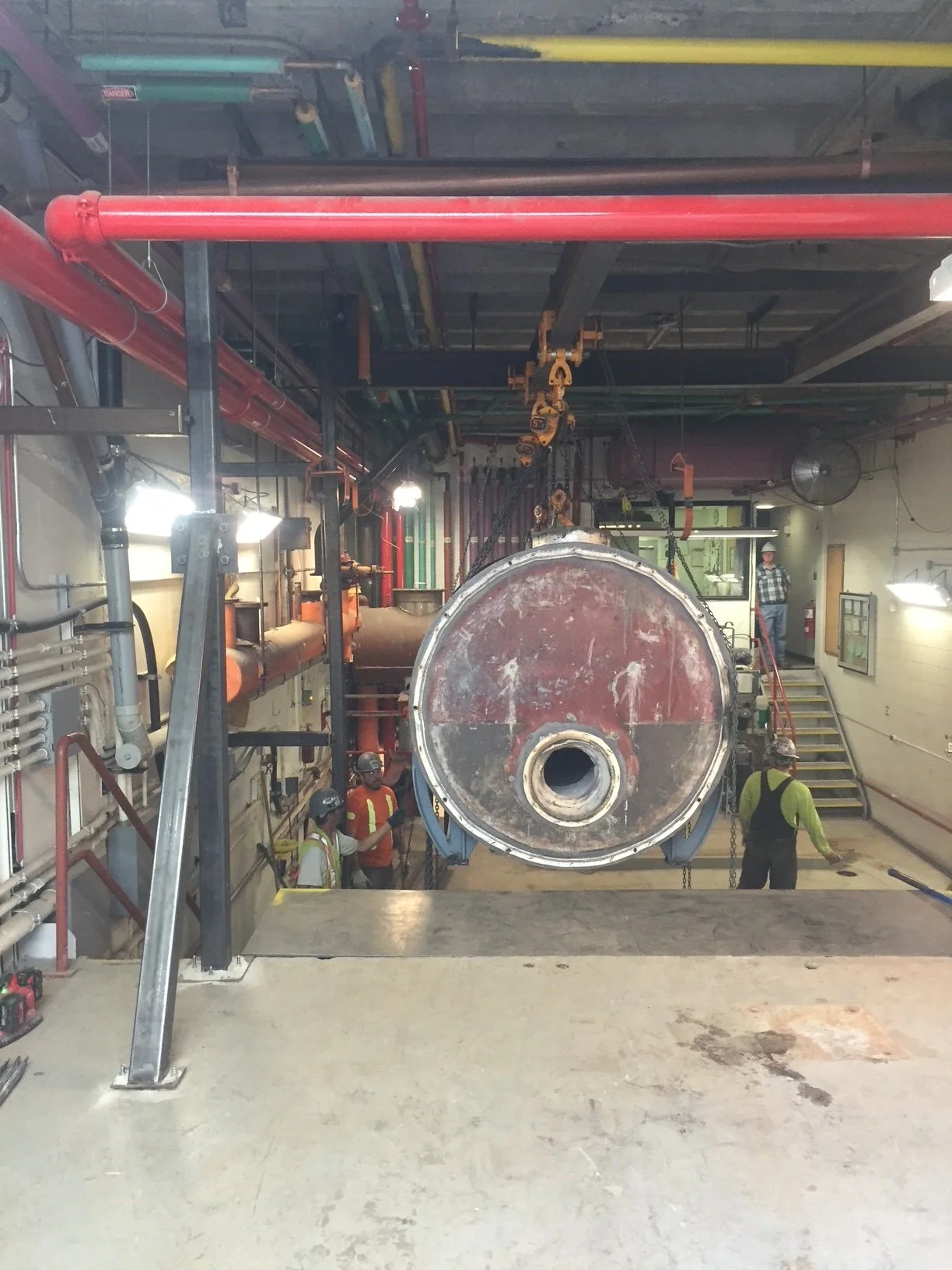Workers inspecting a large industrial boiler or pressure vessel inside a facility with visible pipes and equipment.